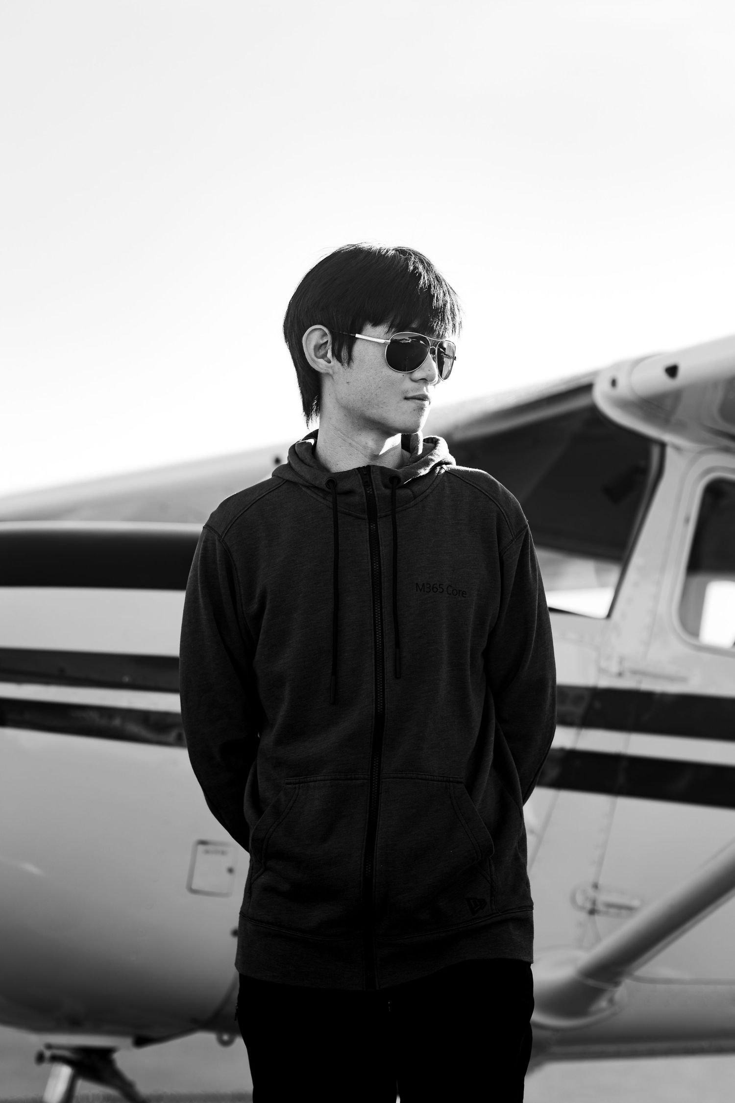 A person in dark clothing and sunglasses stands beside a small private aircraft in a black and white photograph.