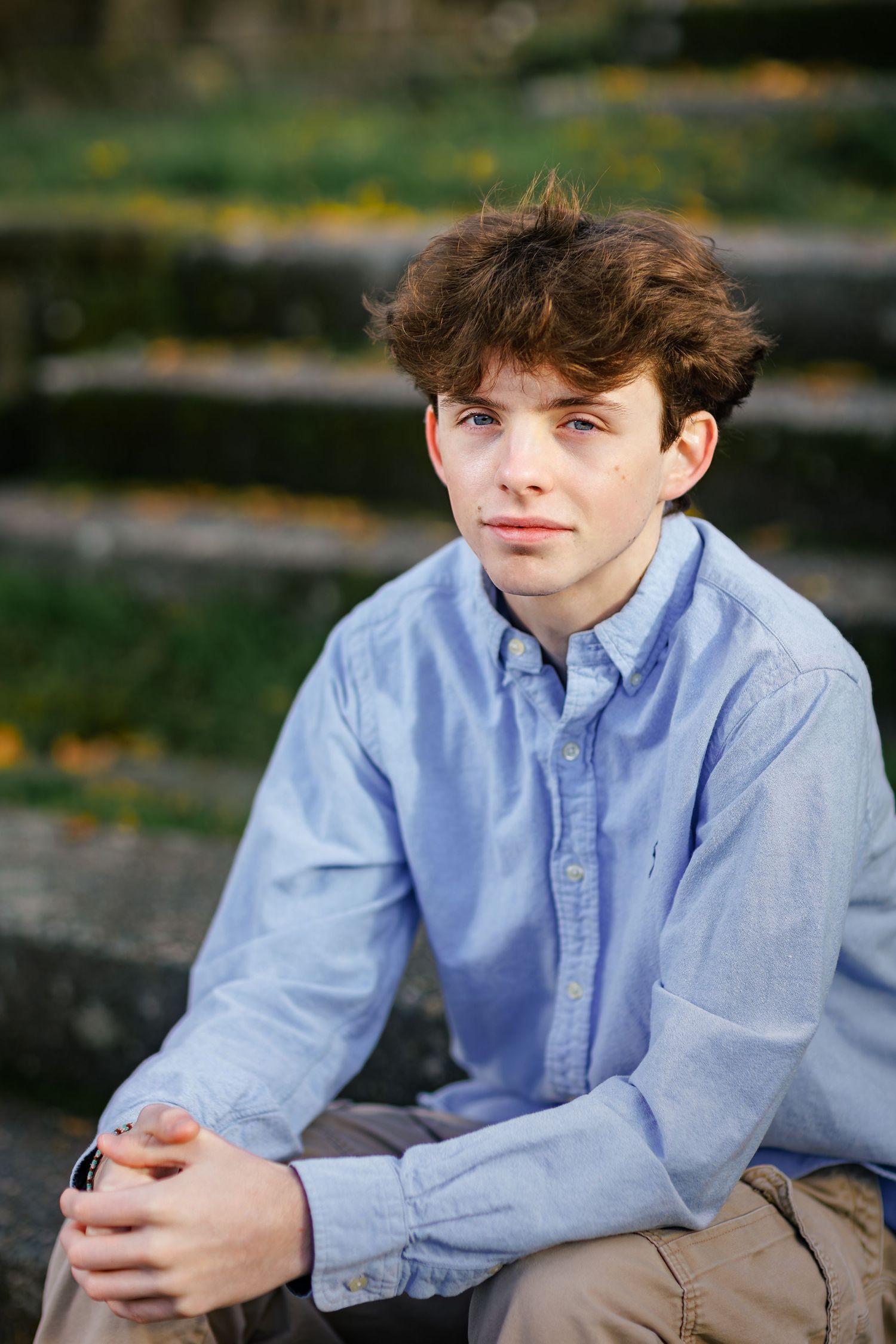 A person in a light blue button-down shirt poses outdoors on stone steps during a portrait photography session.
