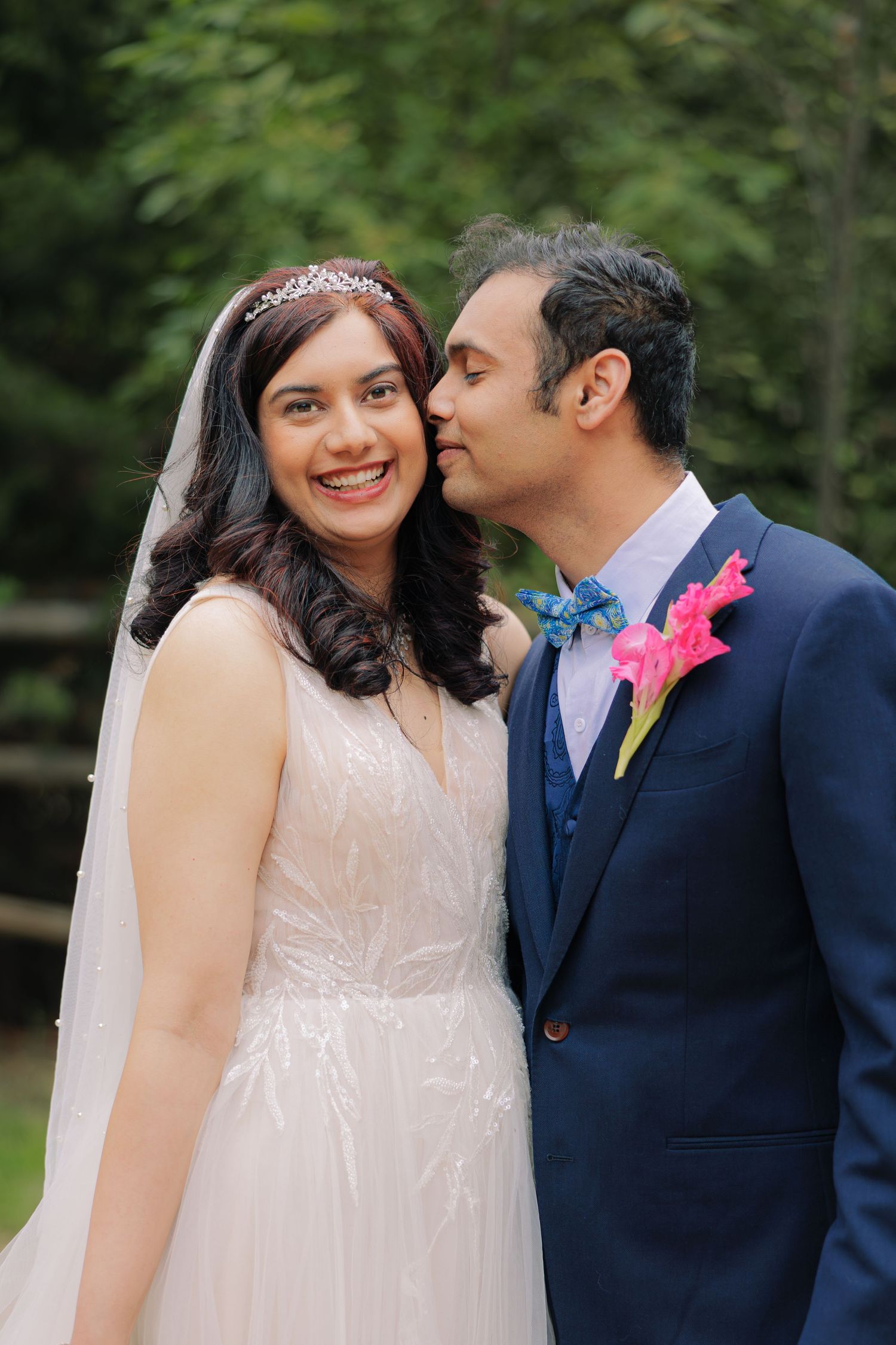A romantic outdoor wedding couple with the groom in navy suit and bright pink boutonniere and bride in a flowing white gown.