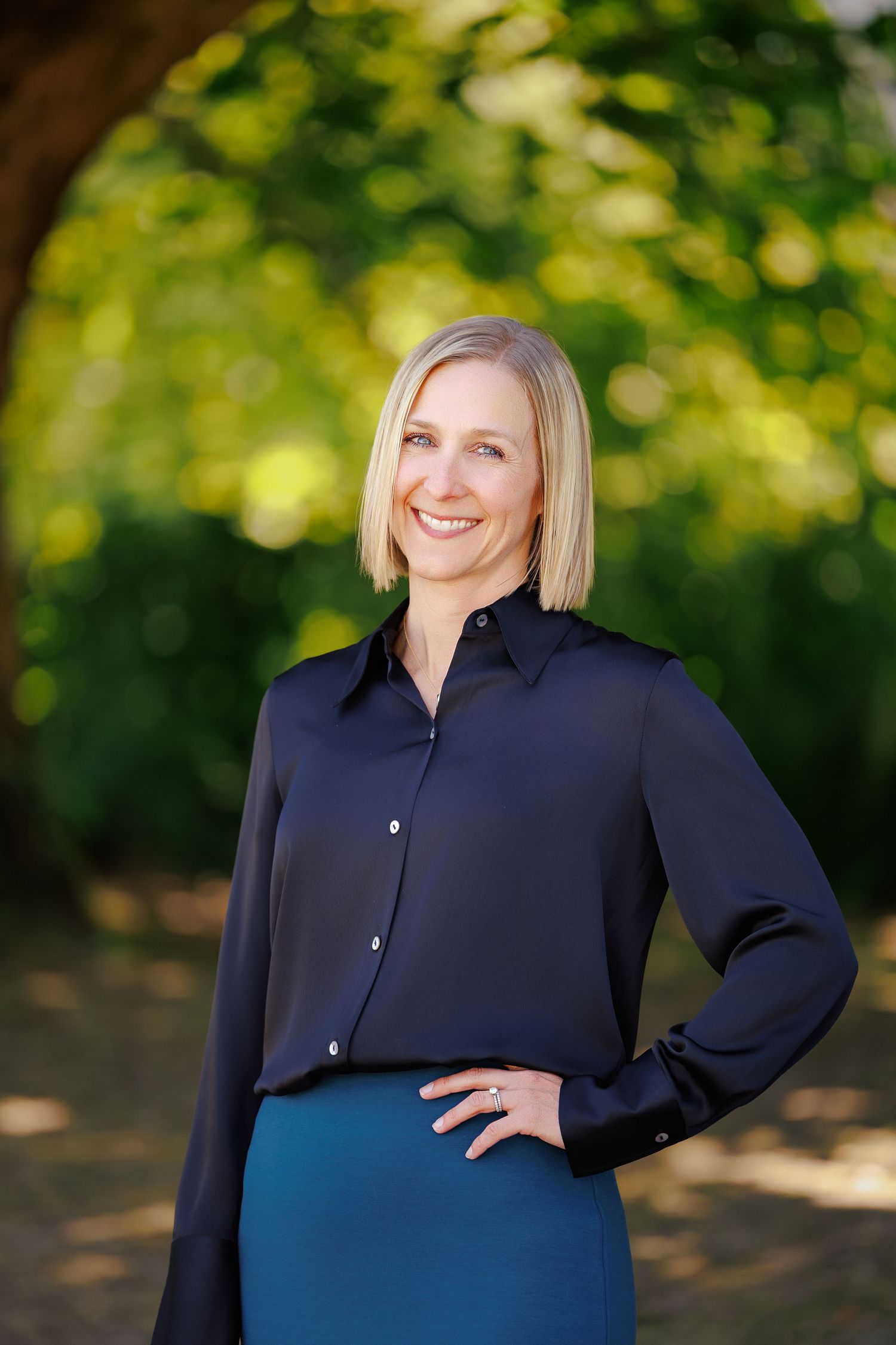 Professional outdoor portrait session with navy blue button-up shirt against blurred green foliage background.