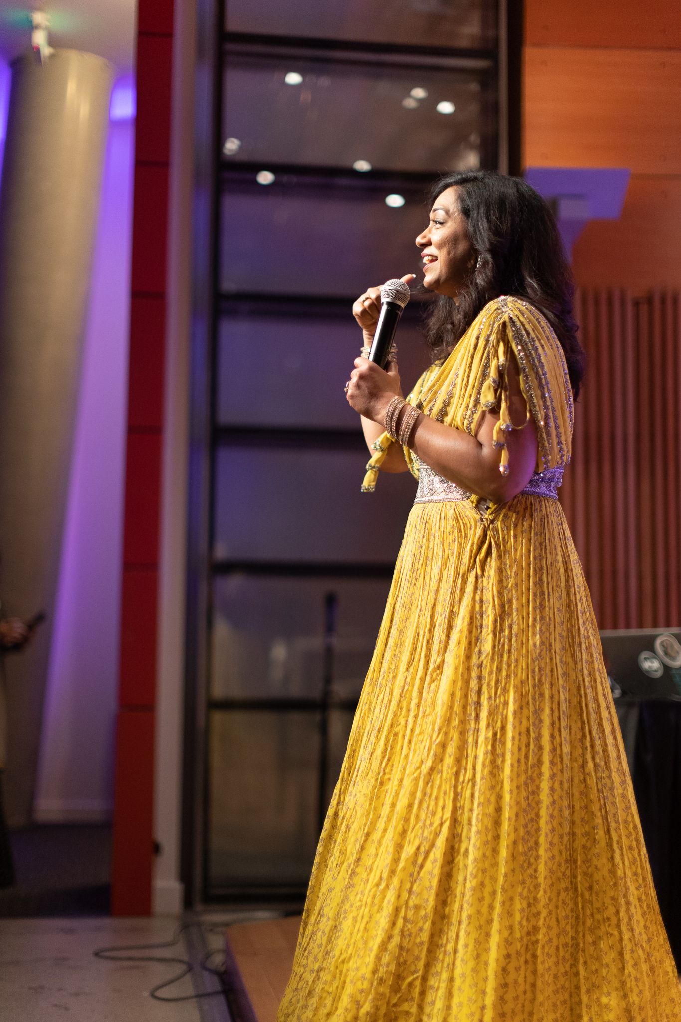 A performer in a yellow sparkly gown sings on stage with dramatic lighting.