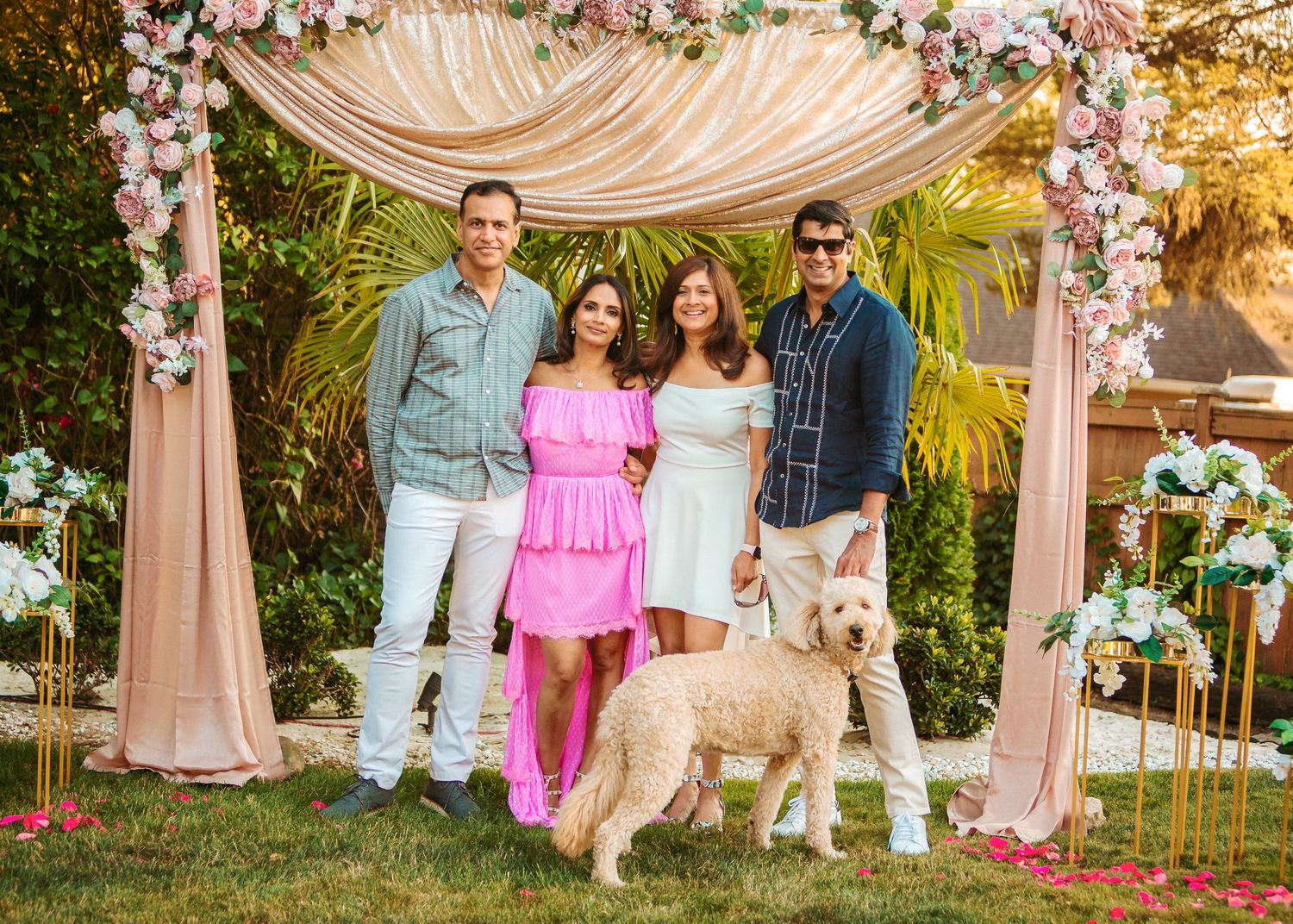 Family poses with their dog under floral wedding arch decorated with pink and white flowers.
