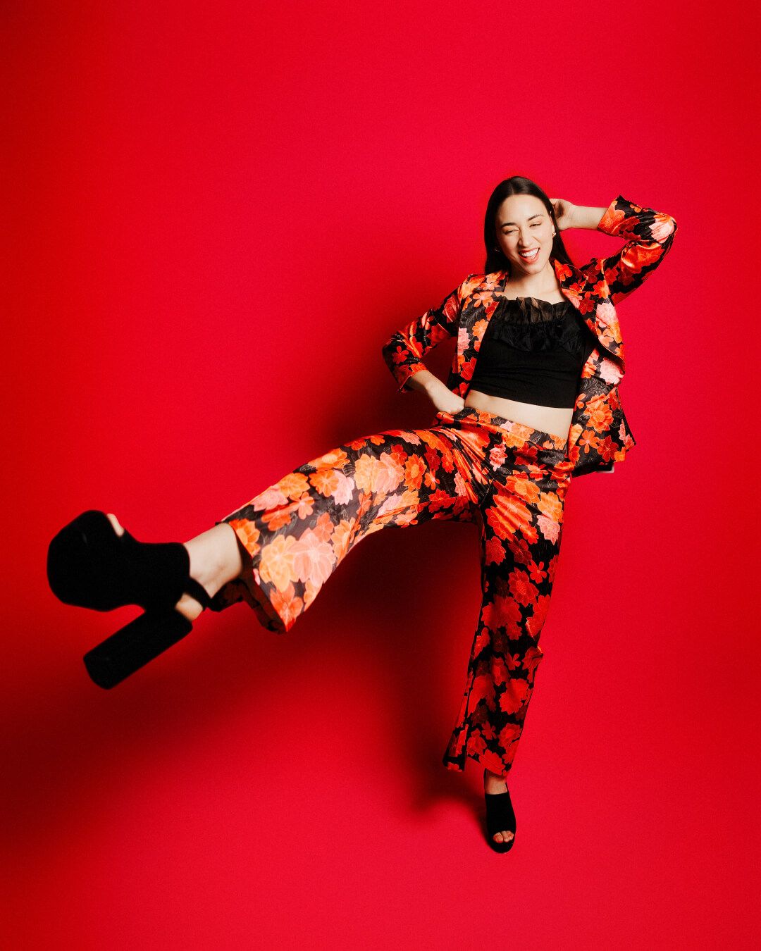 Dancer in floral dress performs dynamic levitation pose against vibrant red backdrop in artistic photo series.