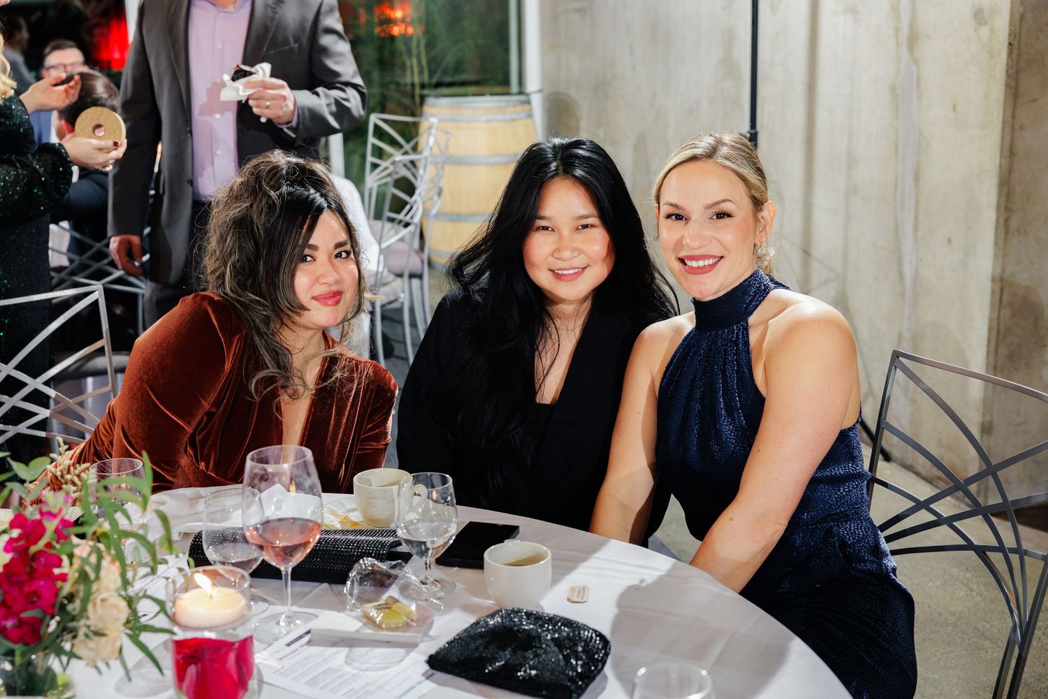 Three friends enjoying drinks and conversation at an elegant dinner table with floral centerpiece.