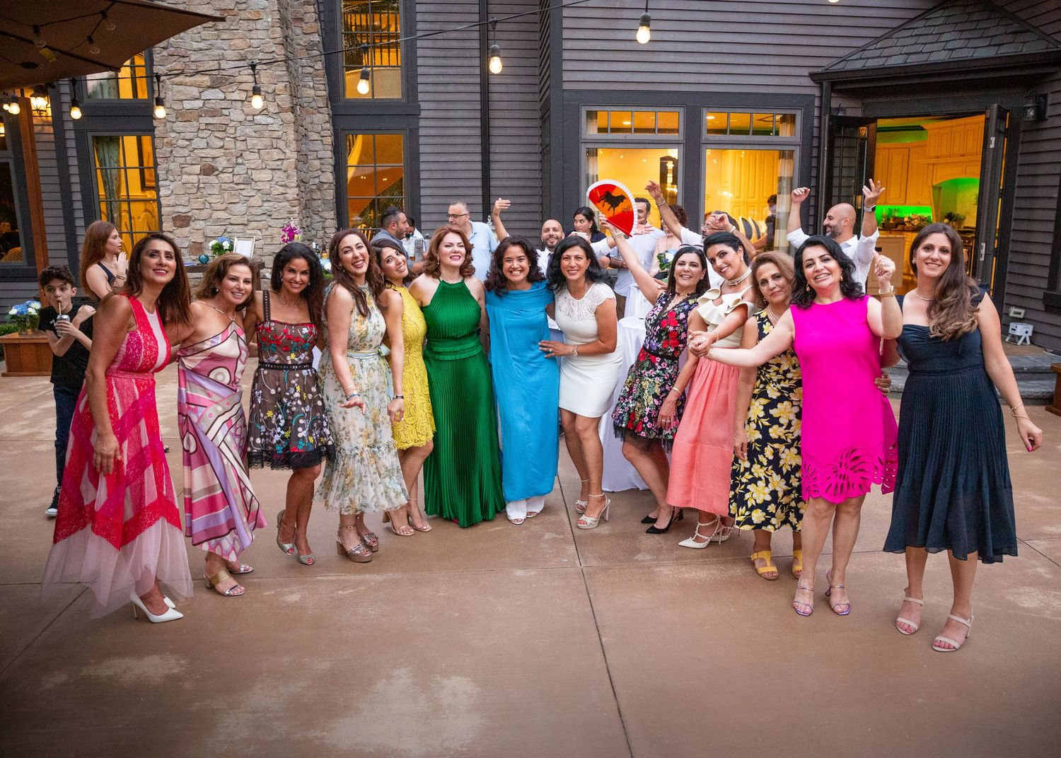 Women in vibrant dresses pose together outside a modern building during a celebration.