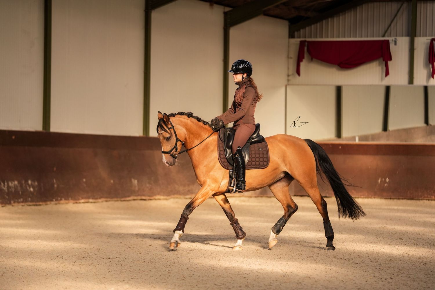 Equestrian riders practice their skills in an indoor arena with multiple horses and riders moving in sequence.