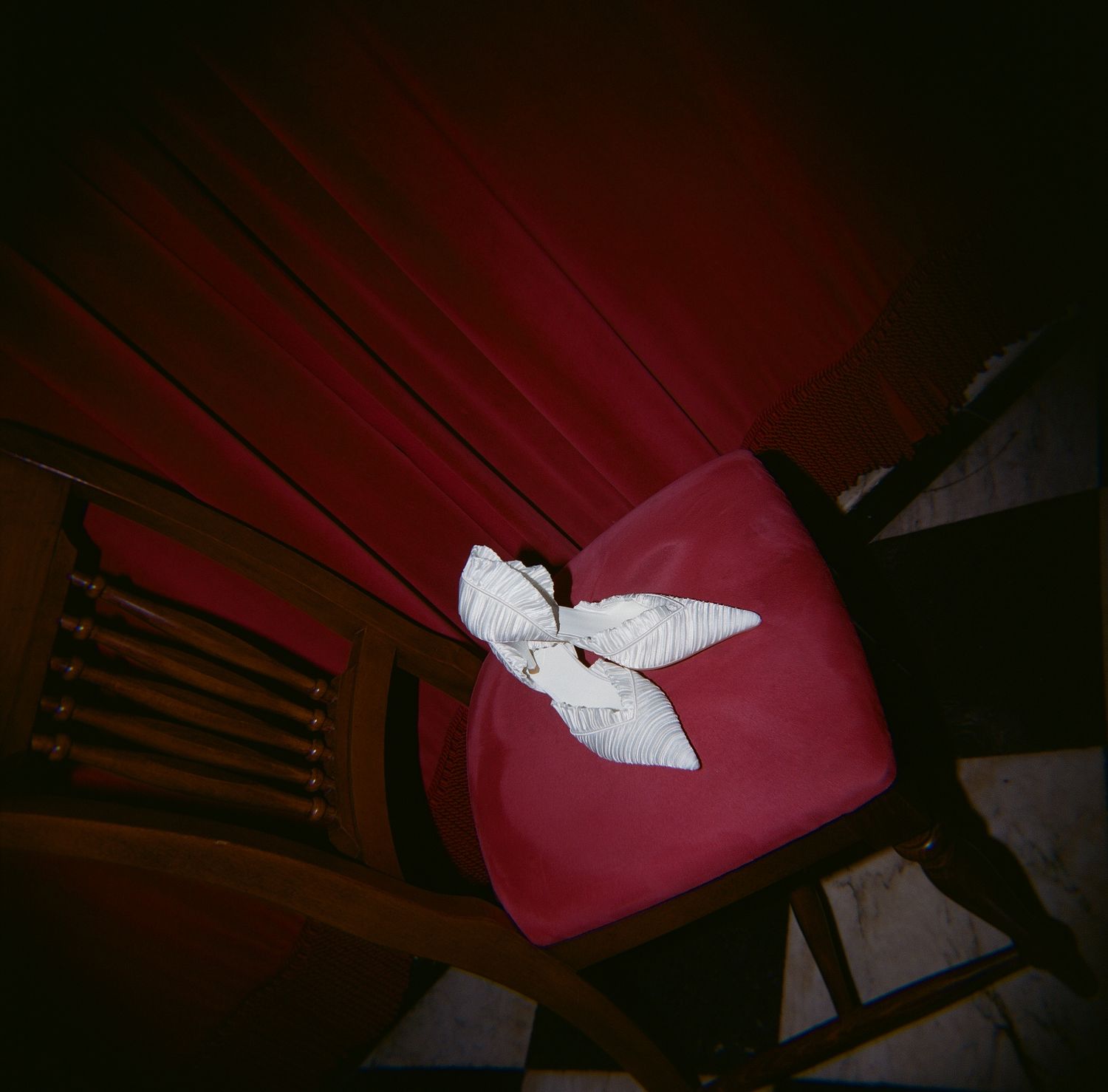 A white bow decorates a deep red chair in dramatic lighting.