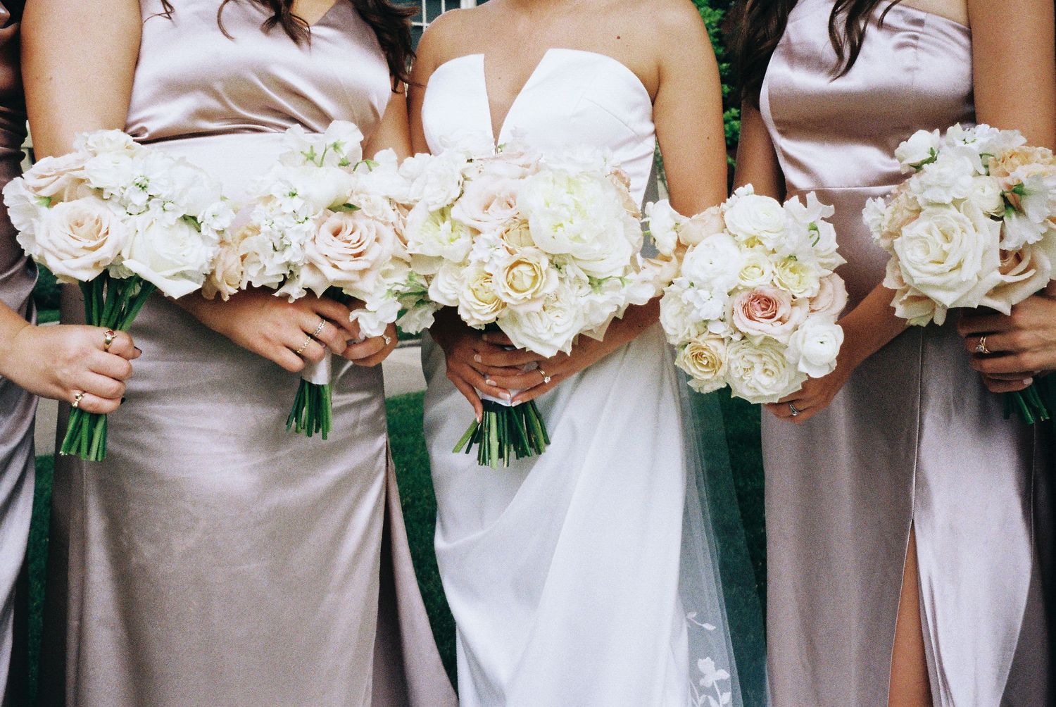 Wedding party holding matching white rose bouquets with satin ribbon wraps.