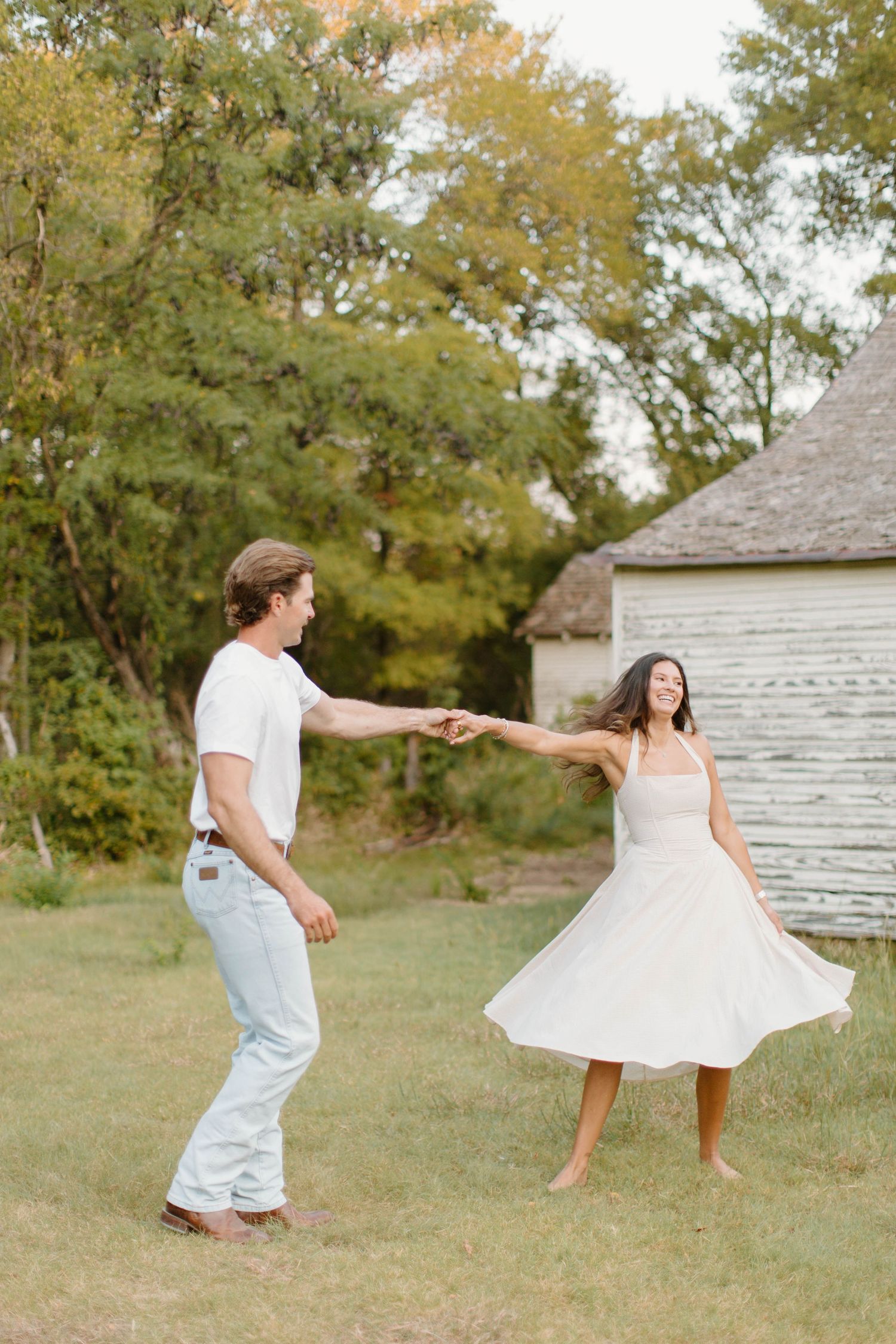 Couple dancing and spinning together in a green outdoor field during engagement session.