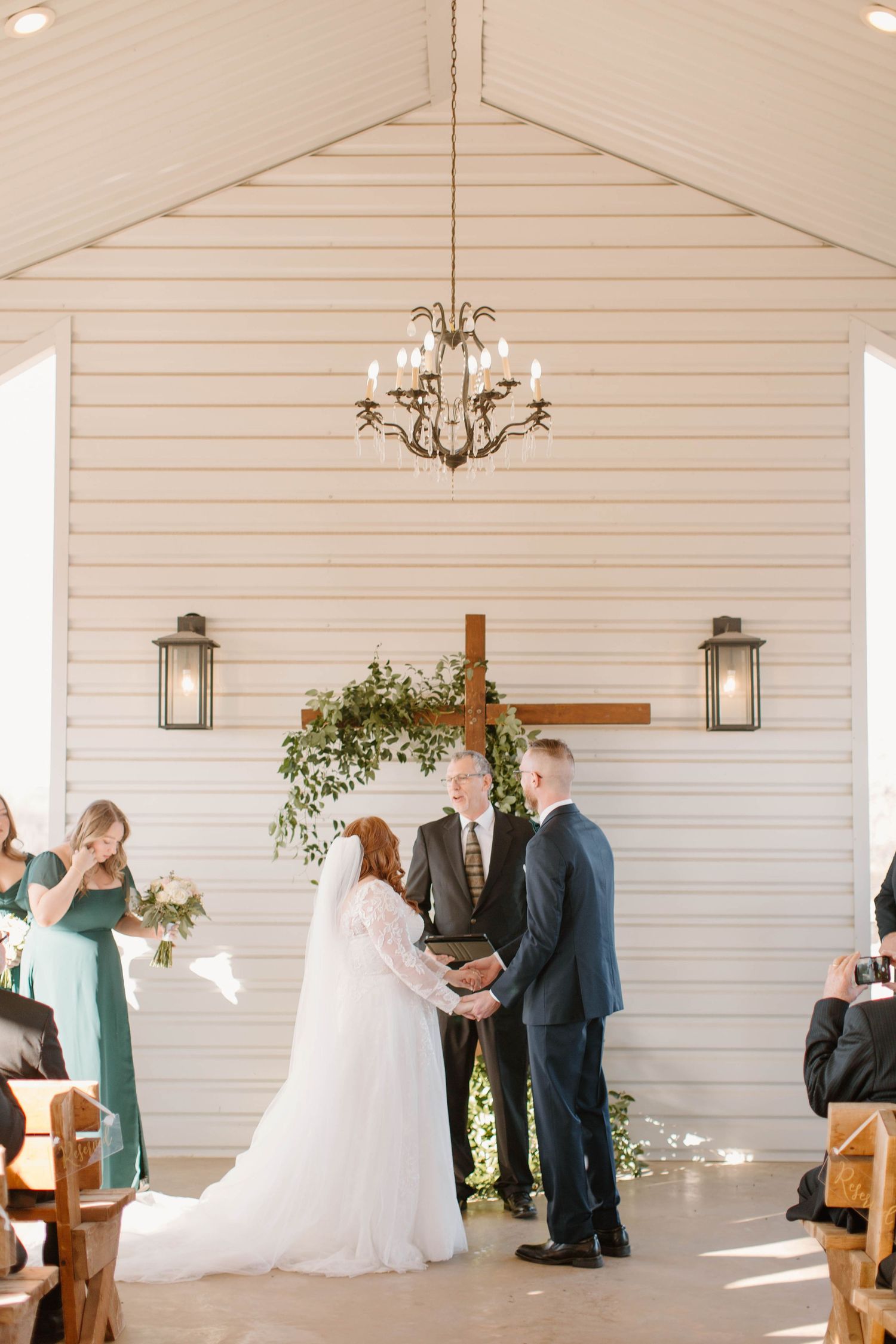 Bride and groom exchanging vows at the altar of a white chapel with wood cross.