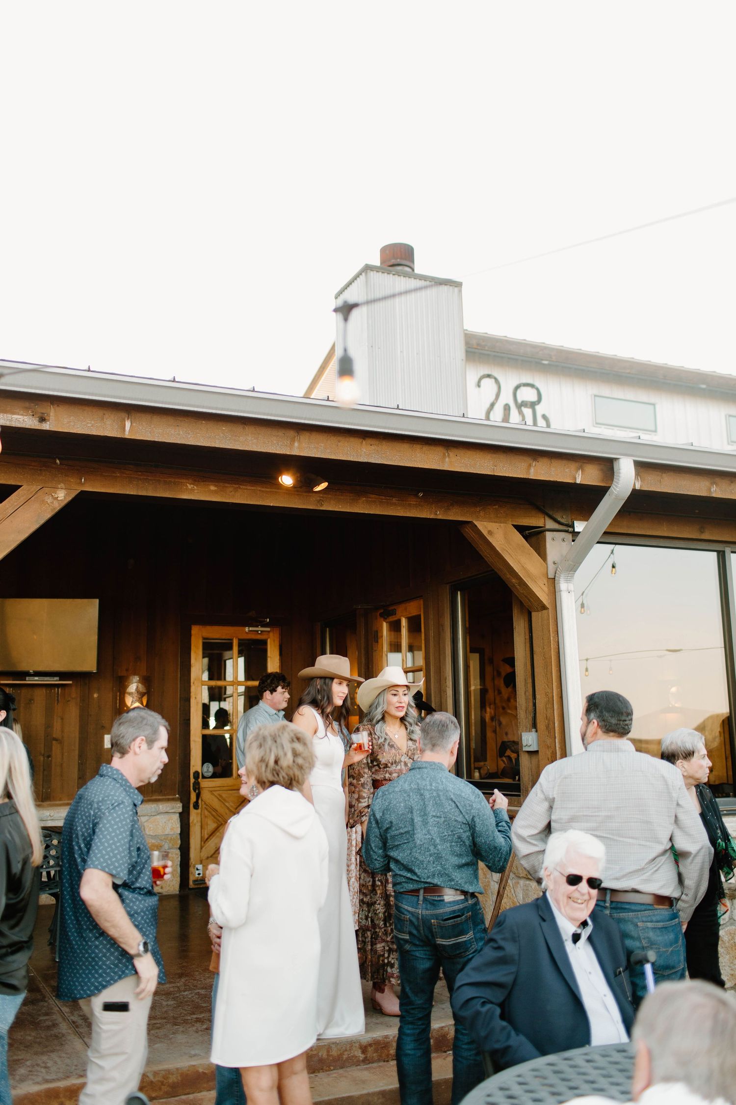 Guests mingling outside a rustic wooden venue building during a western-themed evening event.