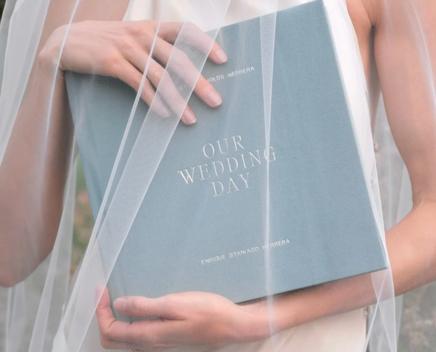 A bride holding a dusty blue wedding day journal covered by a flowing sheer veil.