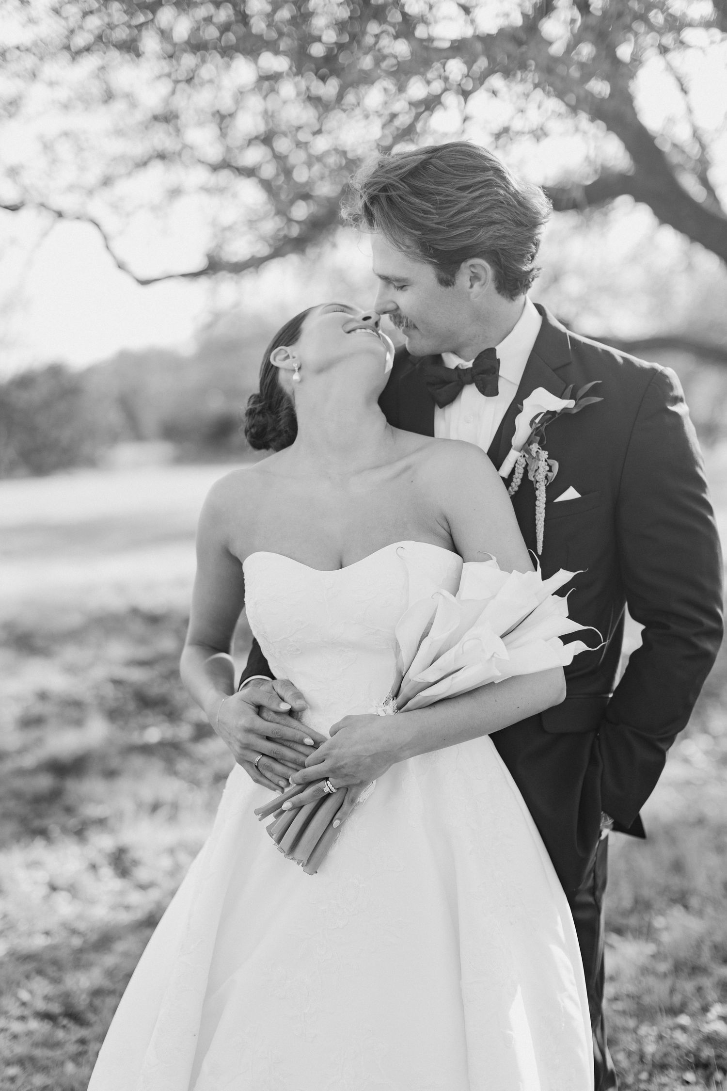 A black and white romantic portrait of a bride and groom sharing a tender moment outdoors.