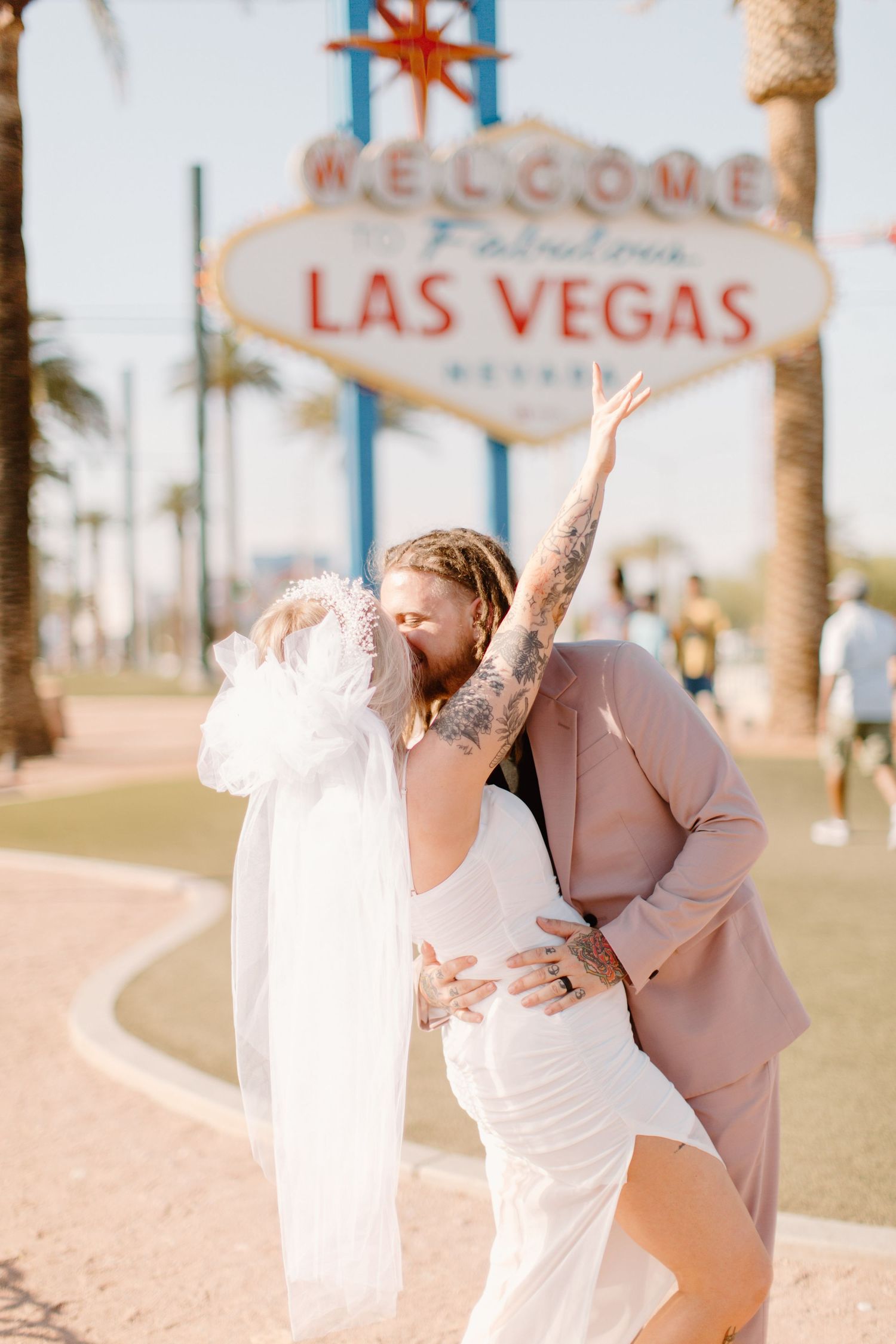 A tattooed couple kisses in wedding attire in front of the Welcome to Las Vegas sign.