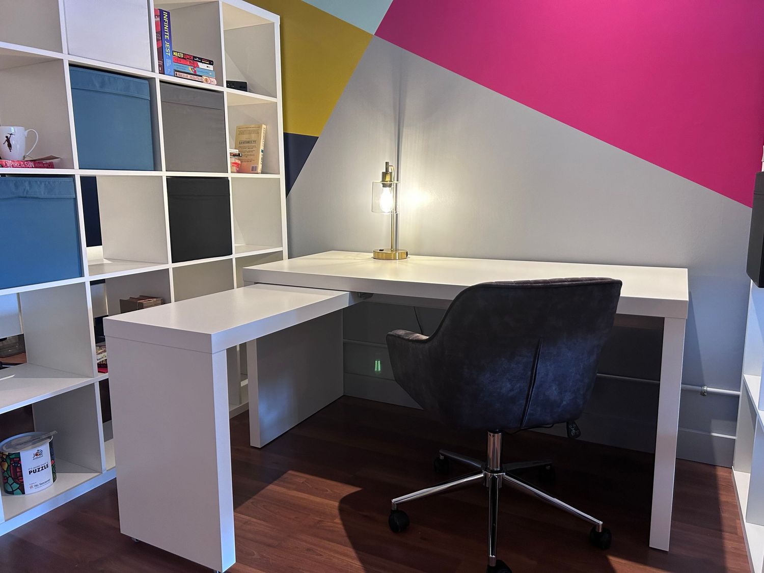 A white desk with velvet rolling desk chair and a colourful mural behind it.