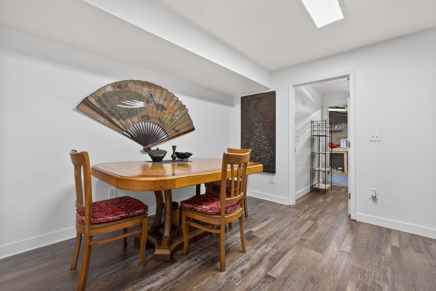Cozy dining room with wooden table, red cushioned chairs, decorative fan wall art, and hardwood floors.