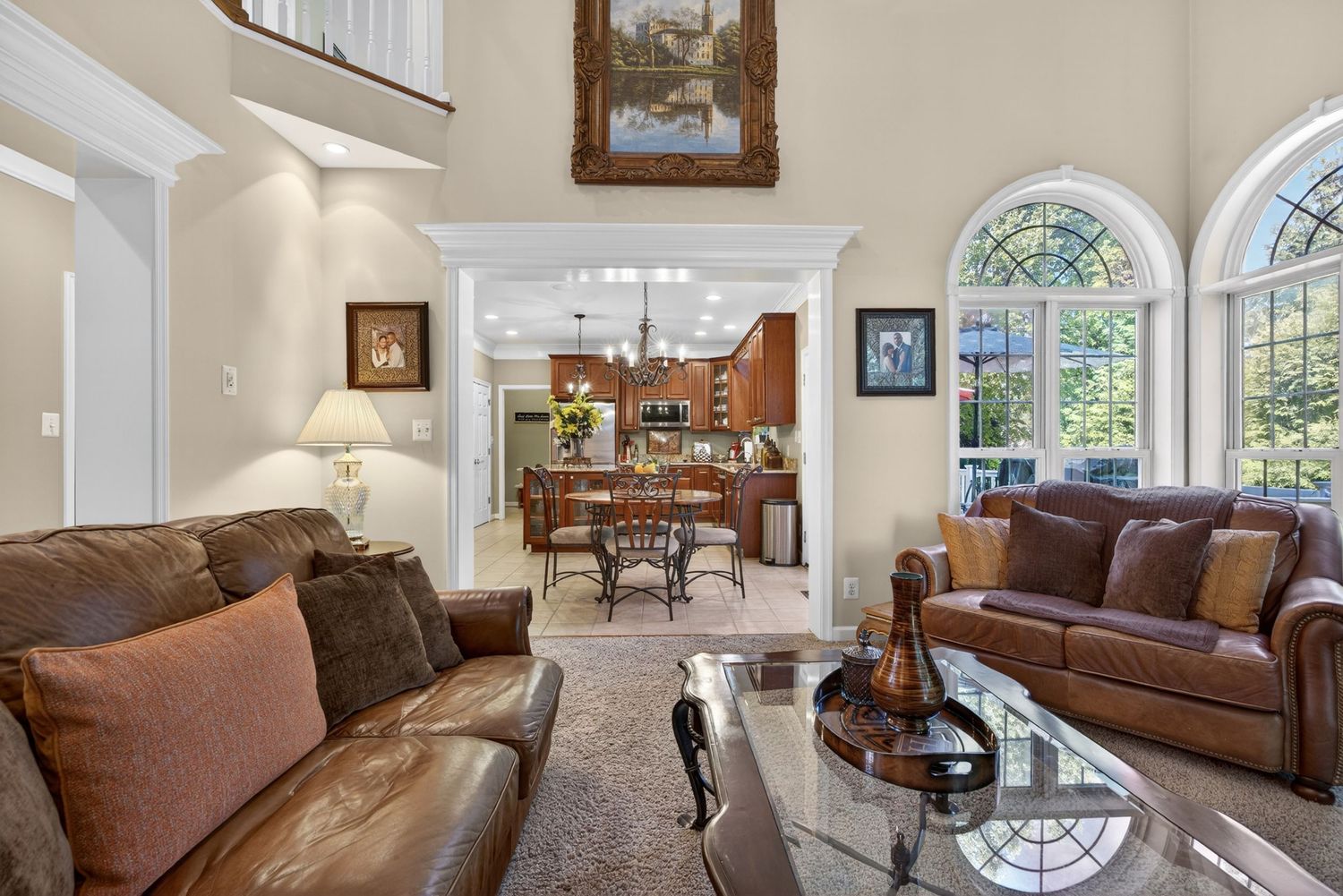 Elegant living room with leather sofas, glass coffee table, arched windows, and open view to dining room and kitchen beyond.