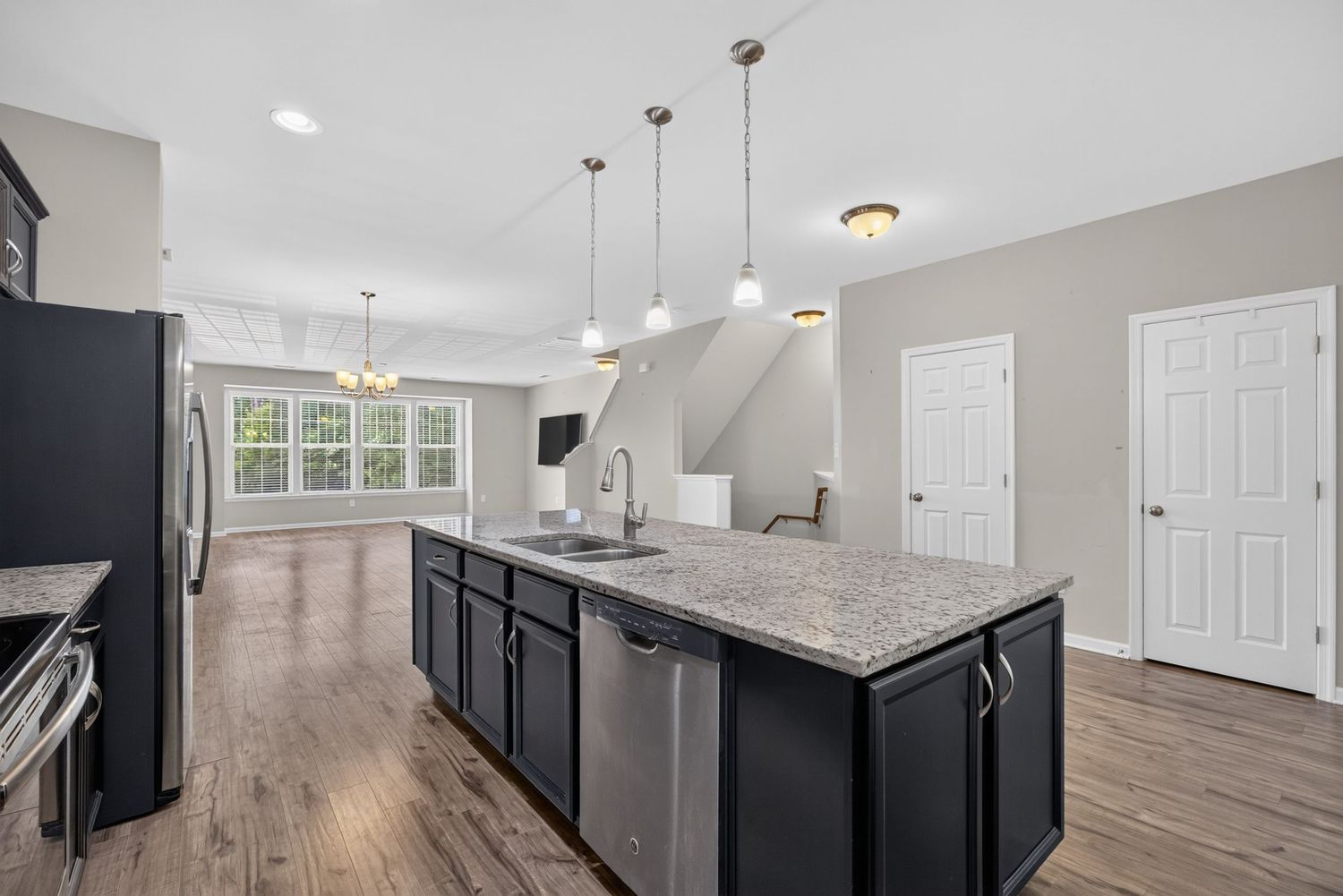Modern kitchen island with dark cabinets, granite countertop, pendant lights, and stainless steel sink overlooking open living area.