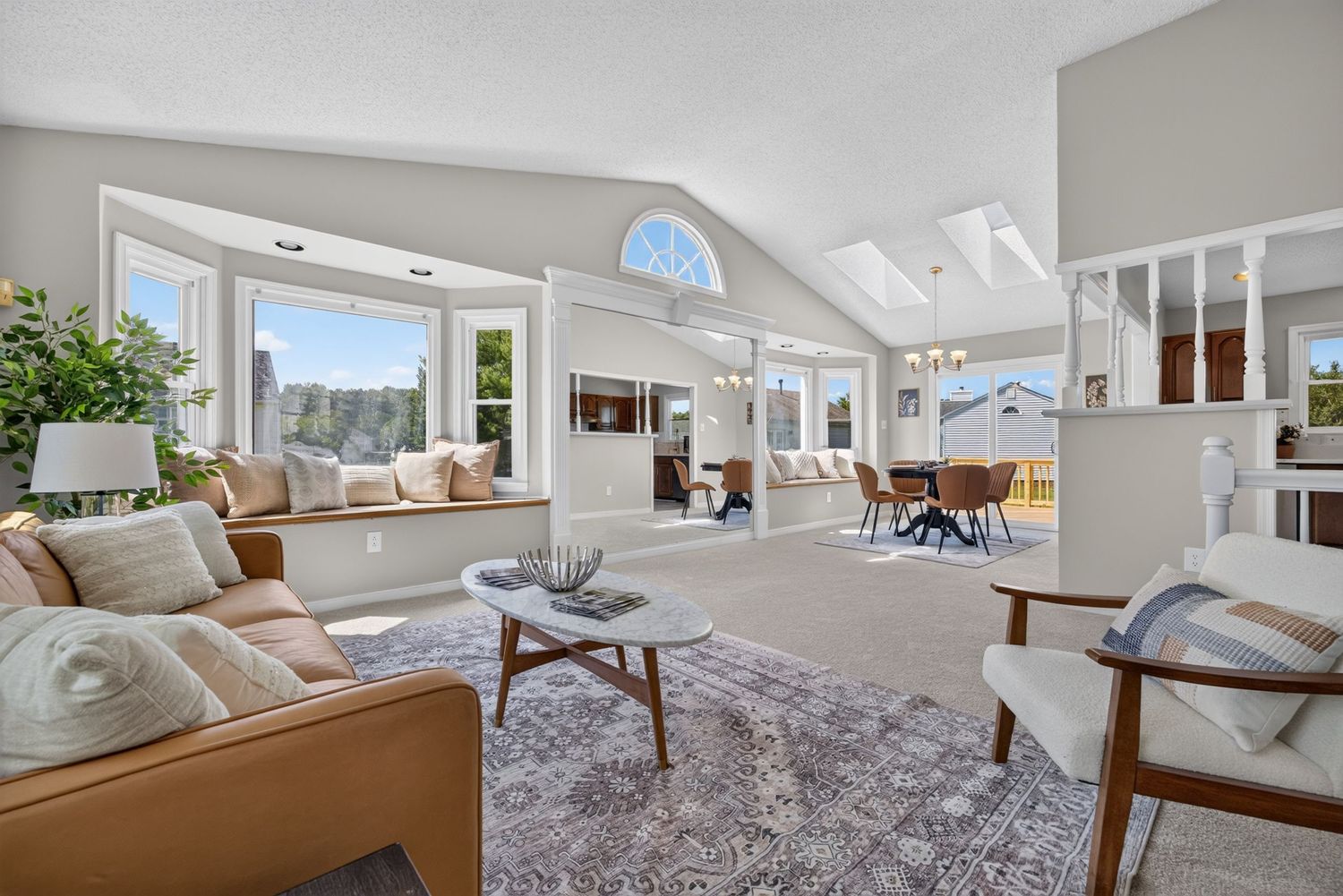 Bright living room with vaulted ceilings, large windows, leather sofa, area rug, and open floor plan with dining area.