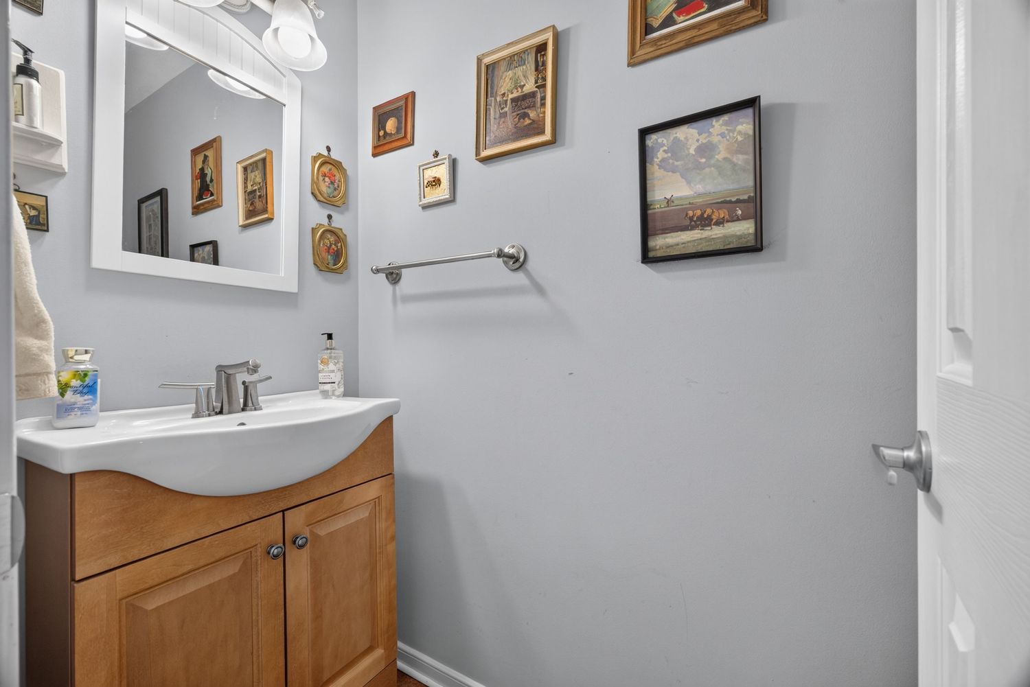 Small bathroom with wooden vanity, white countertop, framed mirror, and decorative wall art on gray walls.