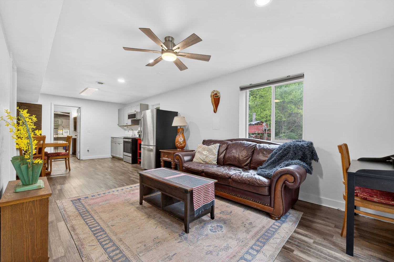 Bright living room with leather sofa, ceiling fan, hardwood floors, and an open view into the kitchen.