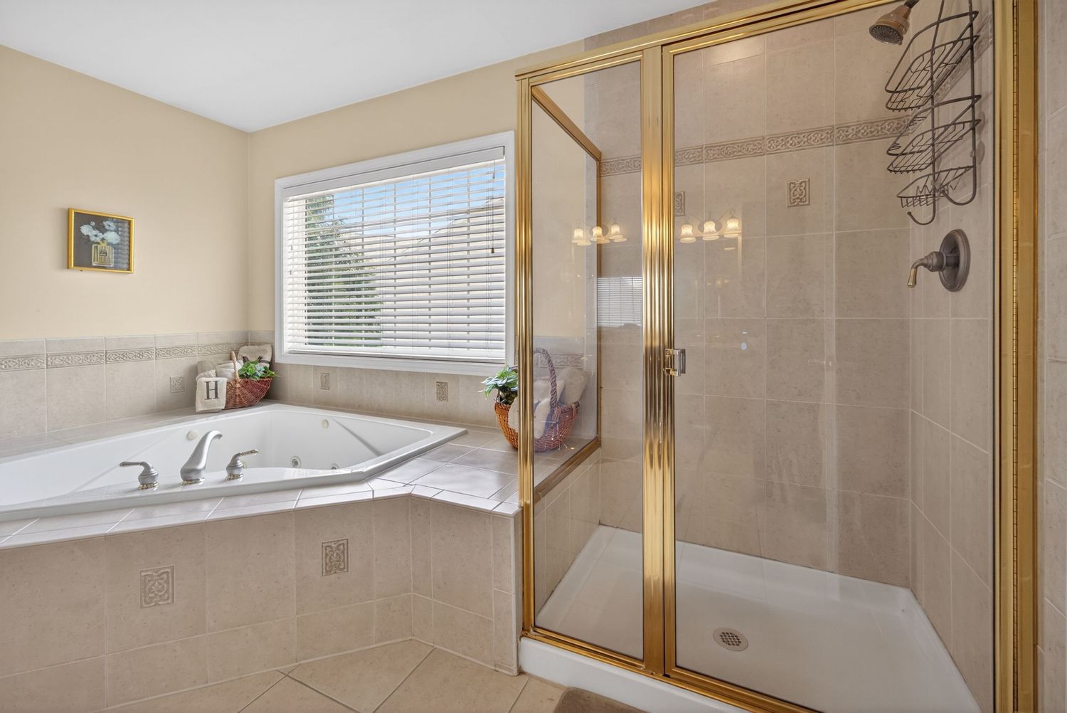 Elegant master bathroom featuring a jetted corner tub and glass-enclosed walk-in shower with gold fixtures.