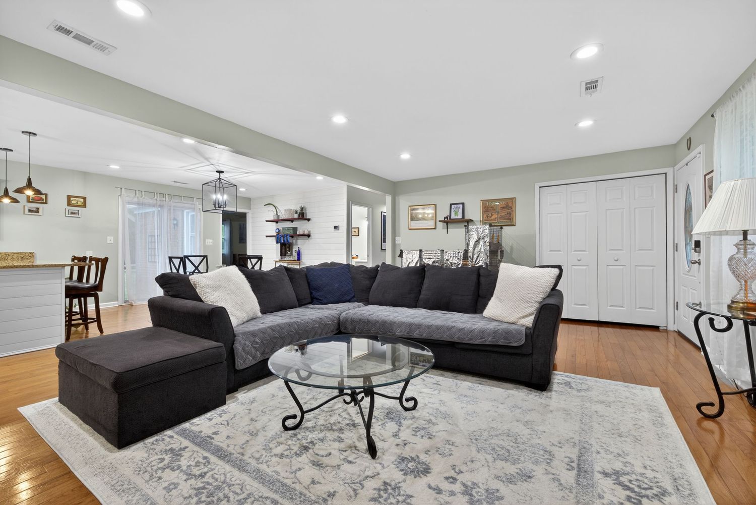 Spacious living room with gray sectional sofa, glass coffee table, hardwood floors, and open floor plan with recessed lighting.
