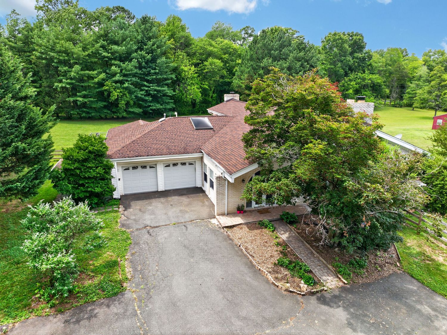 Aerial view of a charming home with a two-car garage, circular driveway, and lush green surroundings.