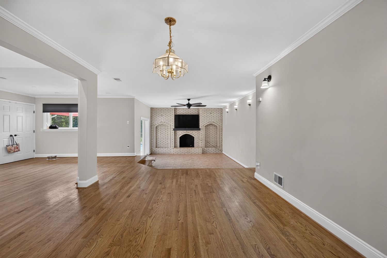 Spacious living room with hardwood floors, brick fireplace, ceiling fan, and elegant chandelier in a bright, open layout.
