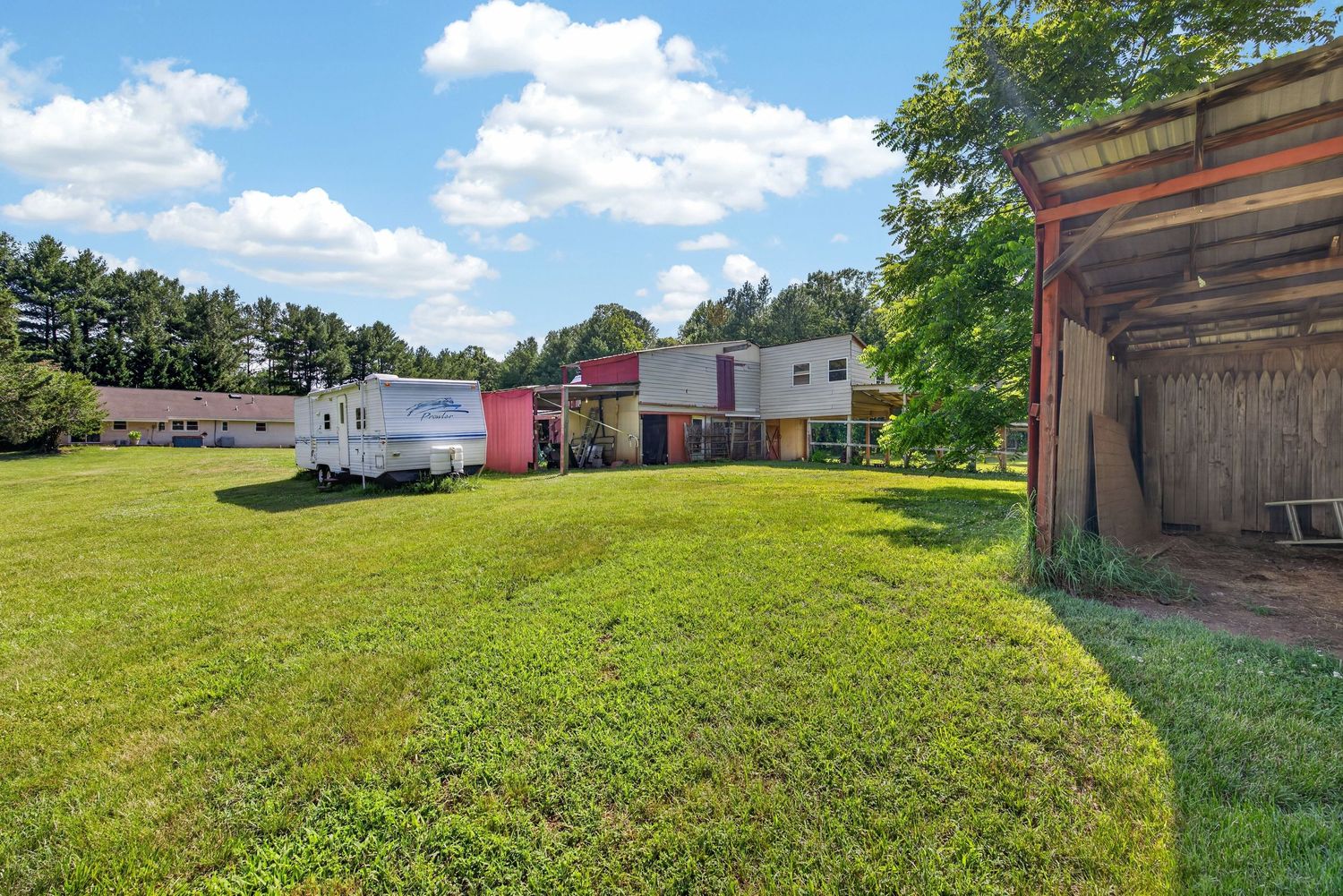 Spacious green lawn with a white RV, two-story home, and wooden shed surrounded by mature trees.