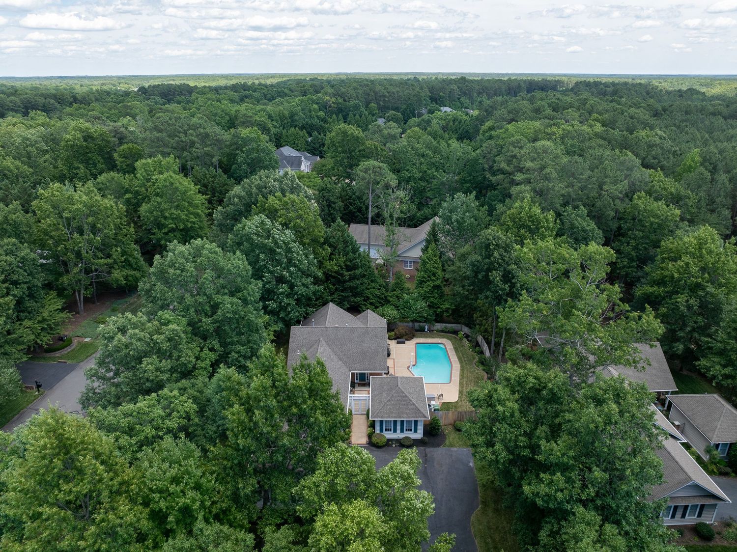 Aerial view of a large suburban home with a swimming pool surrounded by lush green forest trees.