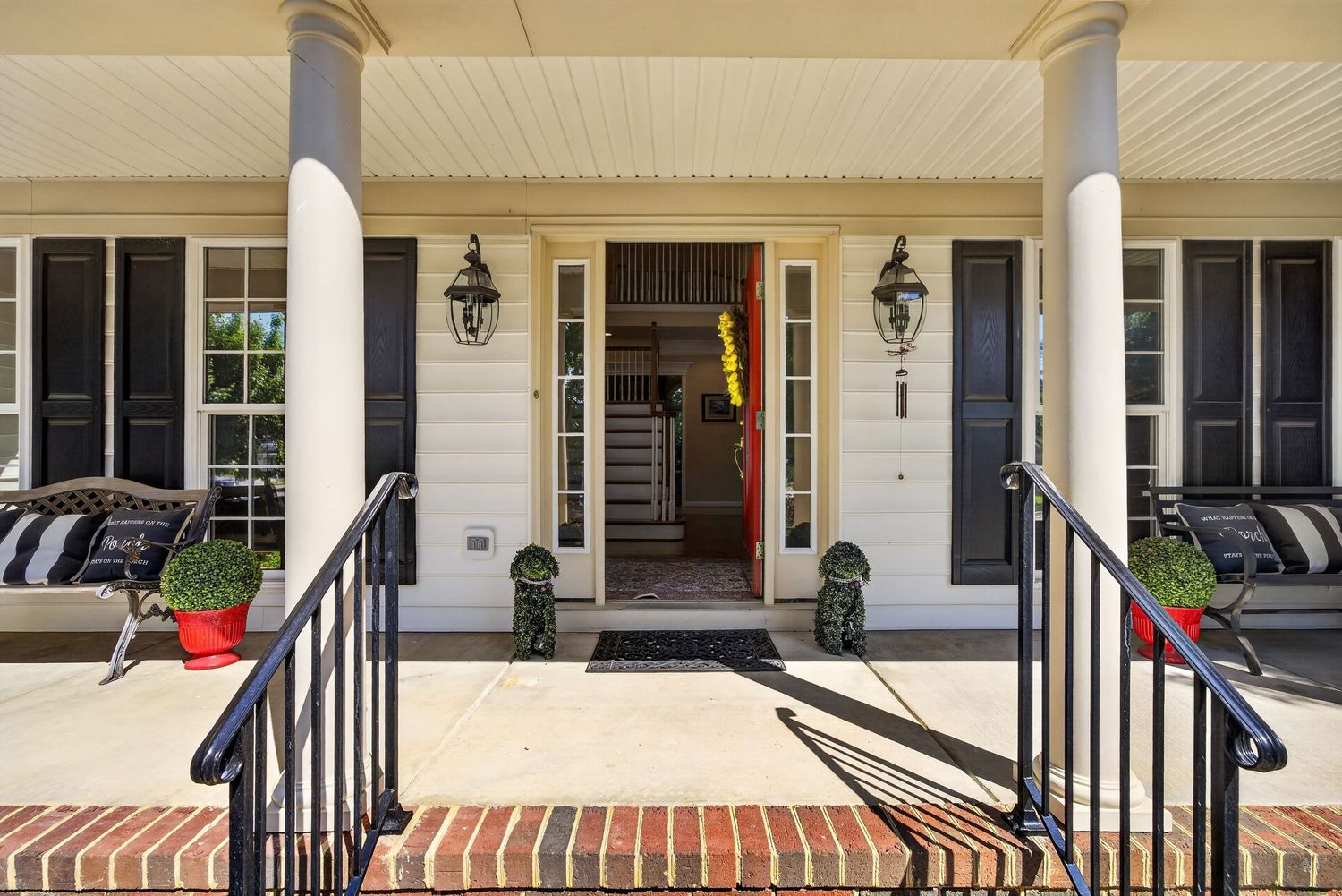 Elegant Southern home front porch with black columns, lantern sconces, brick steps, and black front door with sidelights.