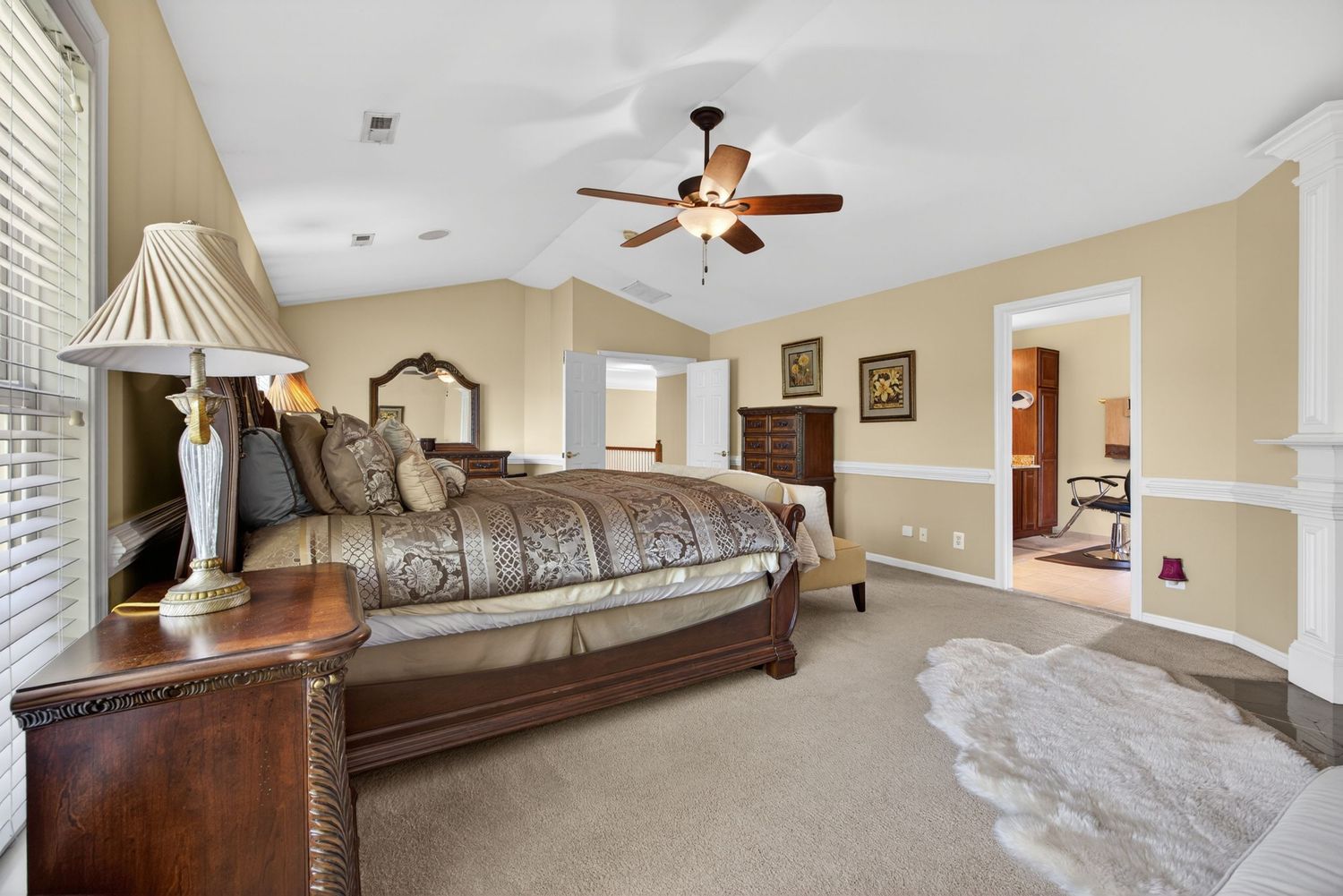 Spacious master bedroom with vaulted ceiling, ceiling fan, hardwood furniture, plush carpet, and an en-suite bathroom.