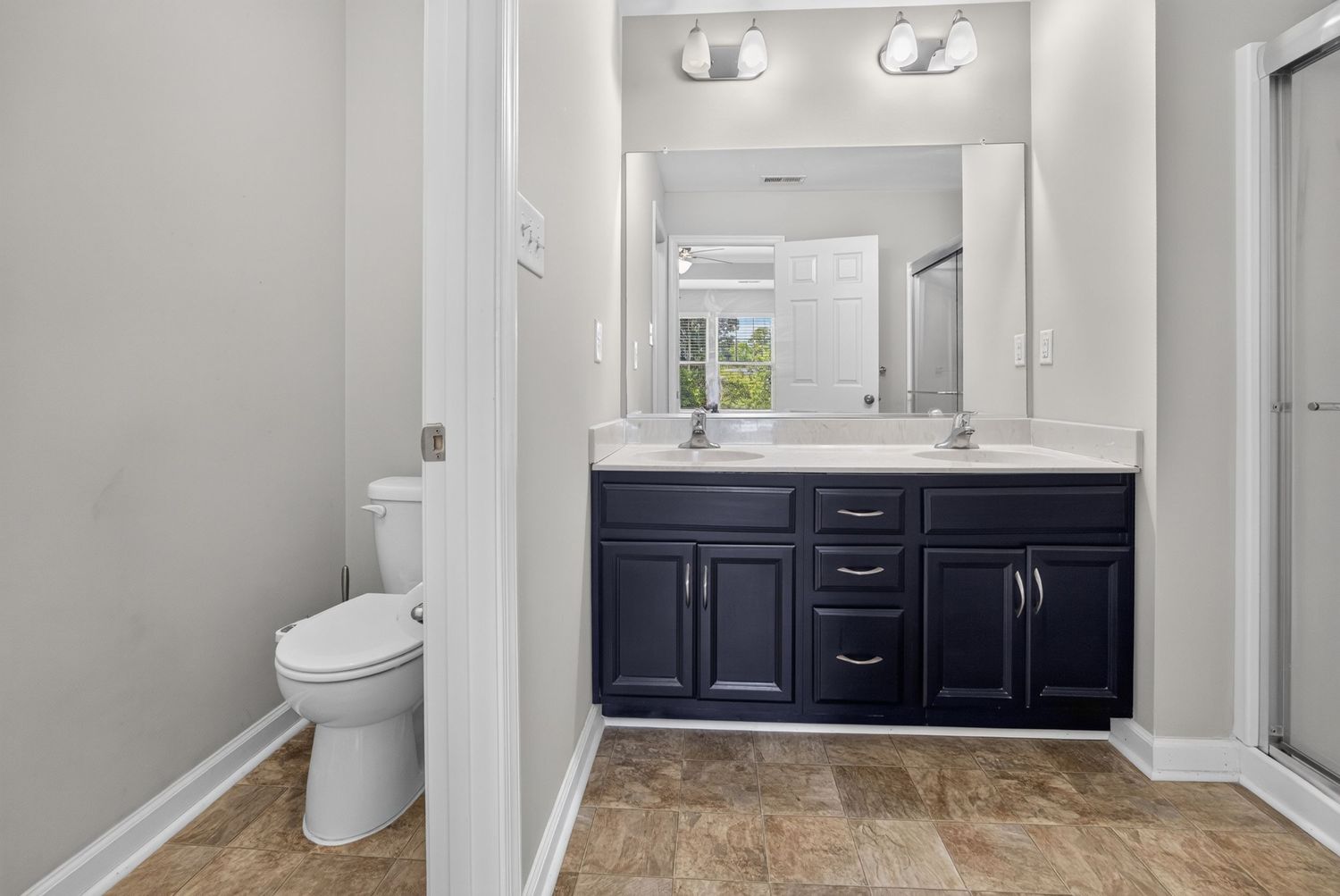 Modern bathroom with navy double vanity, white countertop, large mirror, and tile flooring.