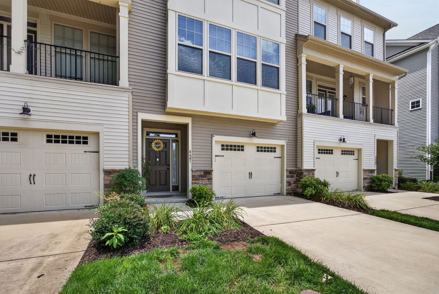 Modern townhome exterior featuring two-car garage, covered balconies, and manicured landscaping with stone accents.