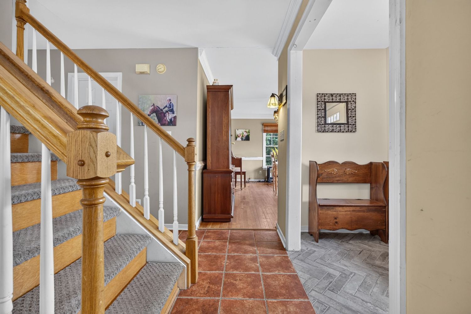 Spacious home entryway with terracotta tile floors, wooden staircase with white balusters, and view into bright living areas.