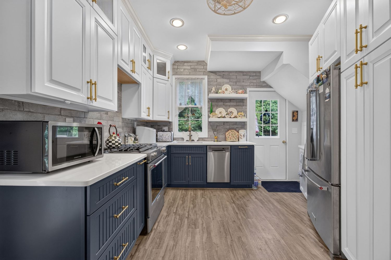 Modern kitchen with navy blue lower cabinets, white upper cabinets, gold hardware, stainless steel appliances, and hardwood floors.