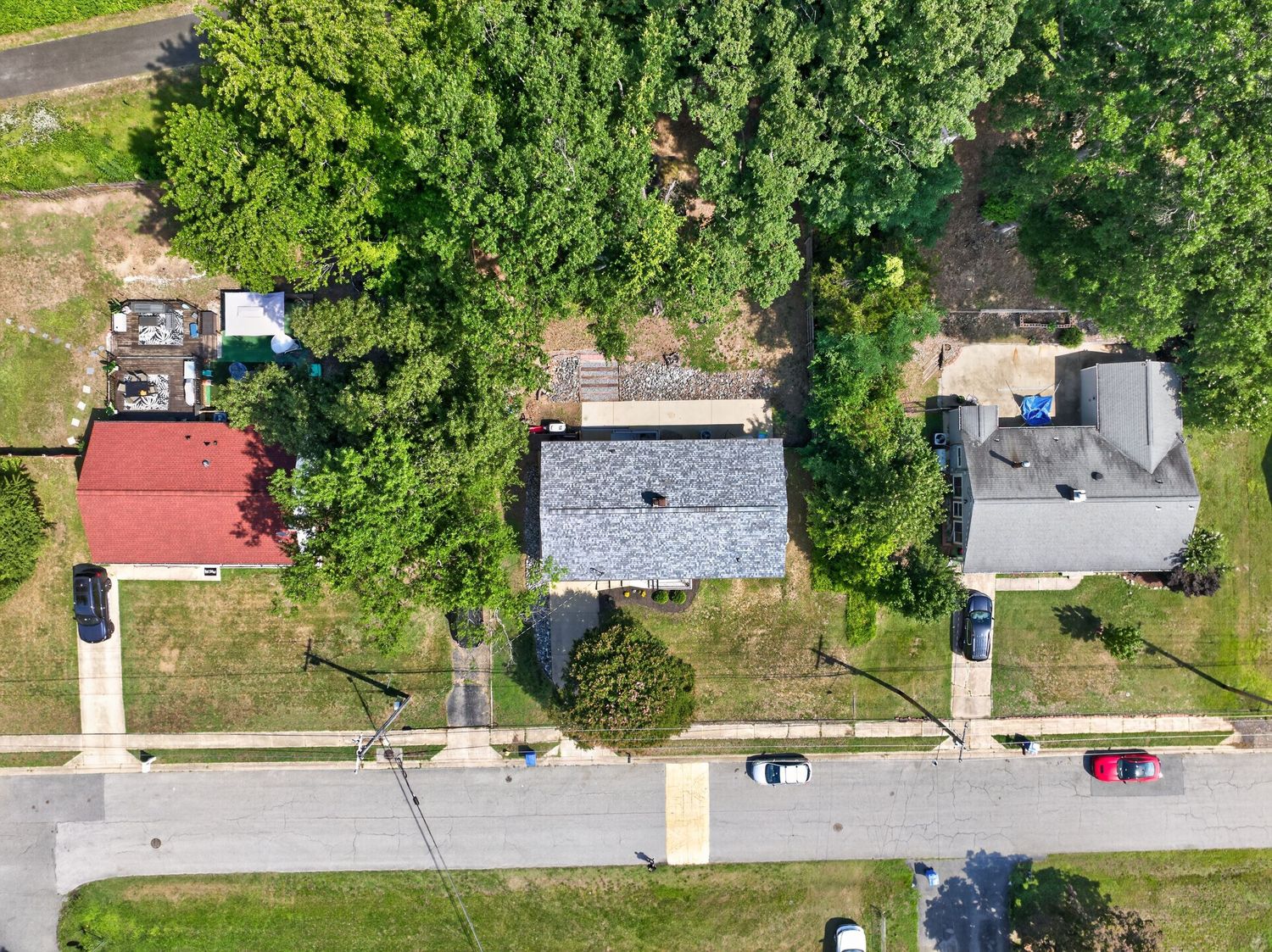 Aerial drone view of residential neighborhood with tree-lined street, small homes, and lush green trees in summer.