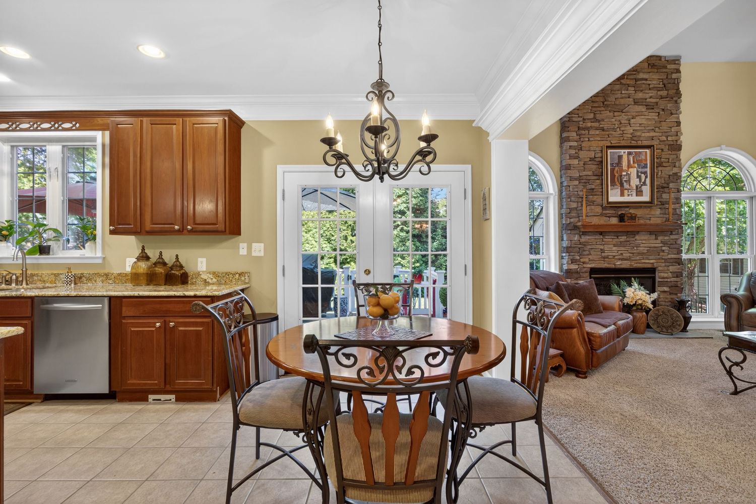 Bright eat-in kitchen with round table, chandelier, cherry cabinets, and open view to stone fireplace living room.