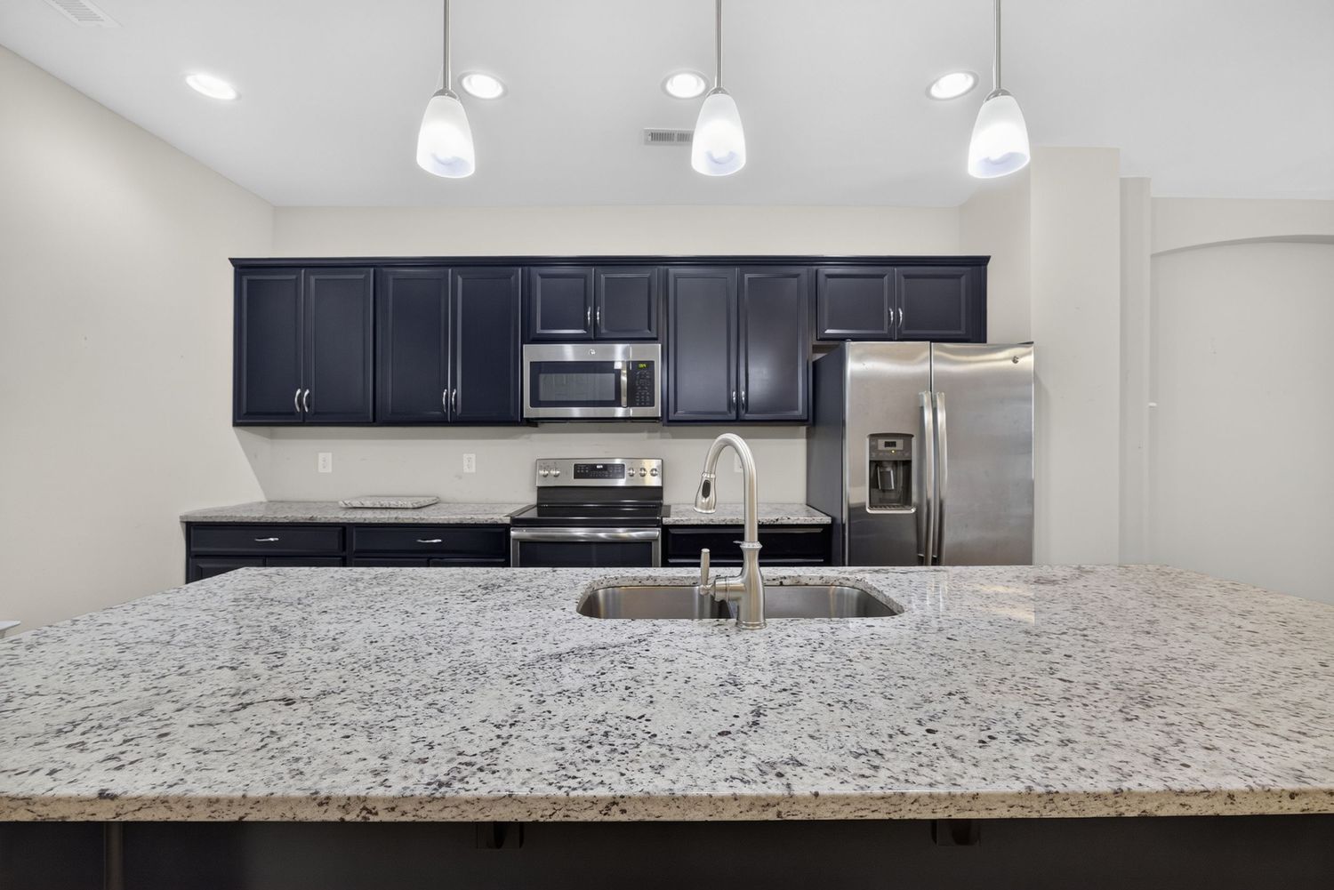 Modern kitchen with dark navy cabinets, granite island, stainless steel appliances, and pendant lighting.