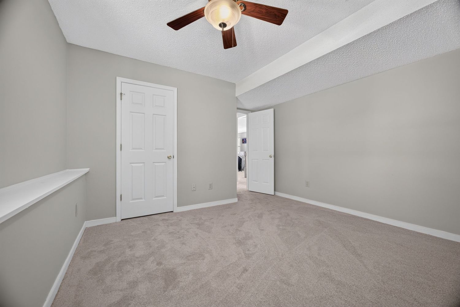 Spacious bedroom with light gray walls, beige carpet, ceiling fan, white doors, and a built-in shelf niche.