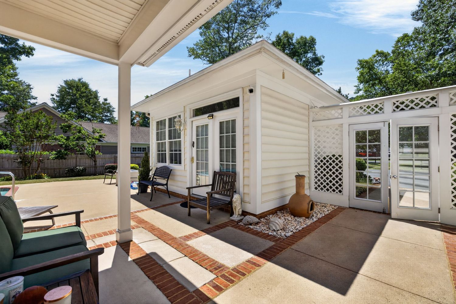 Covered patio with seating area overlooking a charming white guest house with French doors and lattice details.