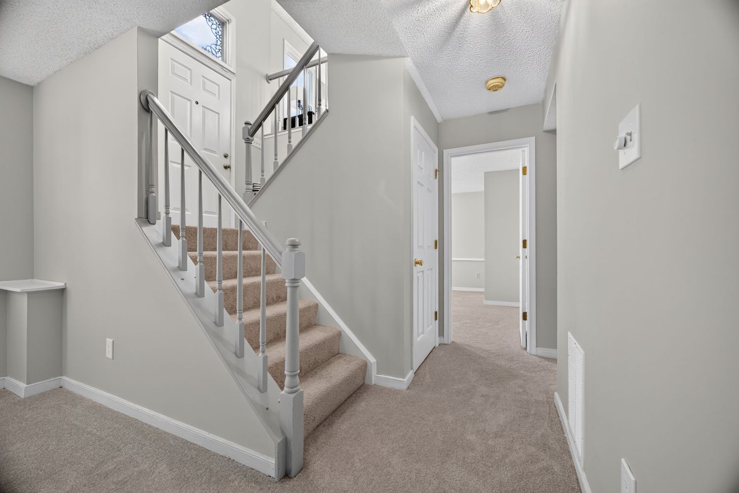 Bright hallway with carpeted staircase, gray metal balusters, white walls, and neutral carpet flooring in a modern home.