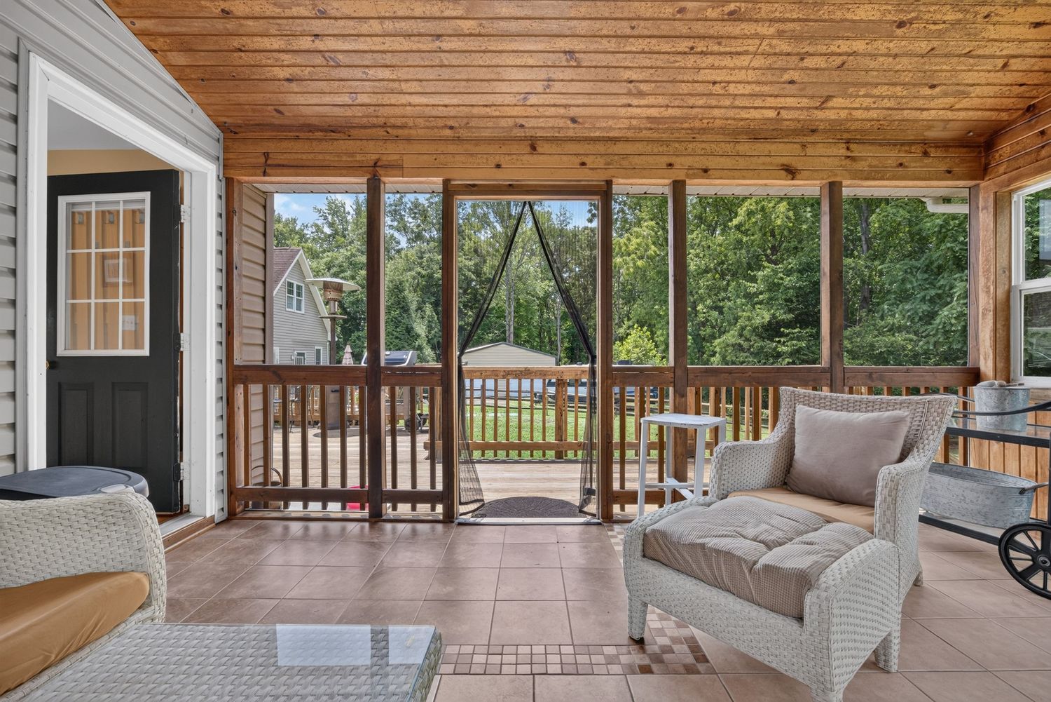 Screened porch with white wicker furniture, tile flooring, wood ceiling, and views of a lush green backyard.