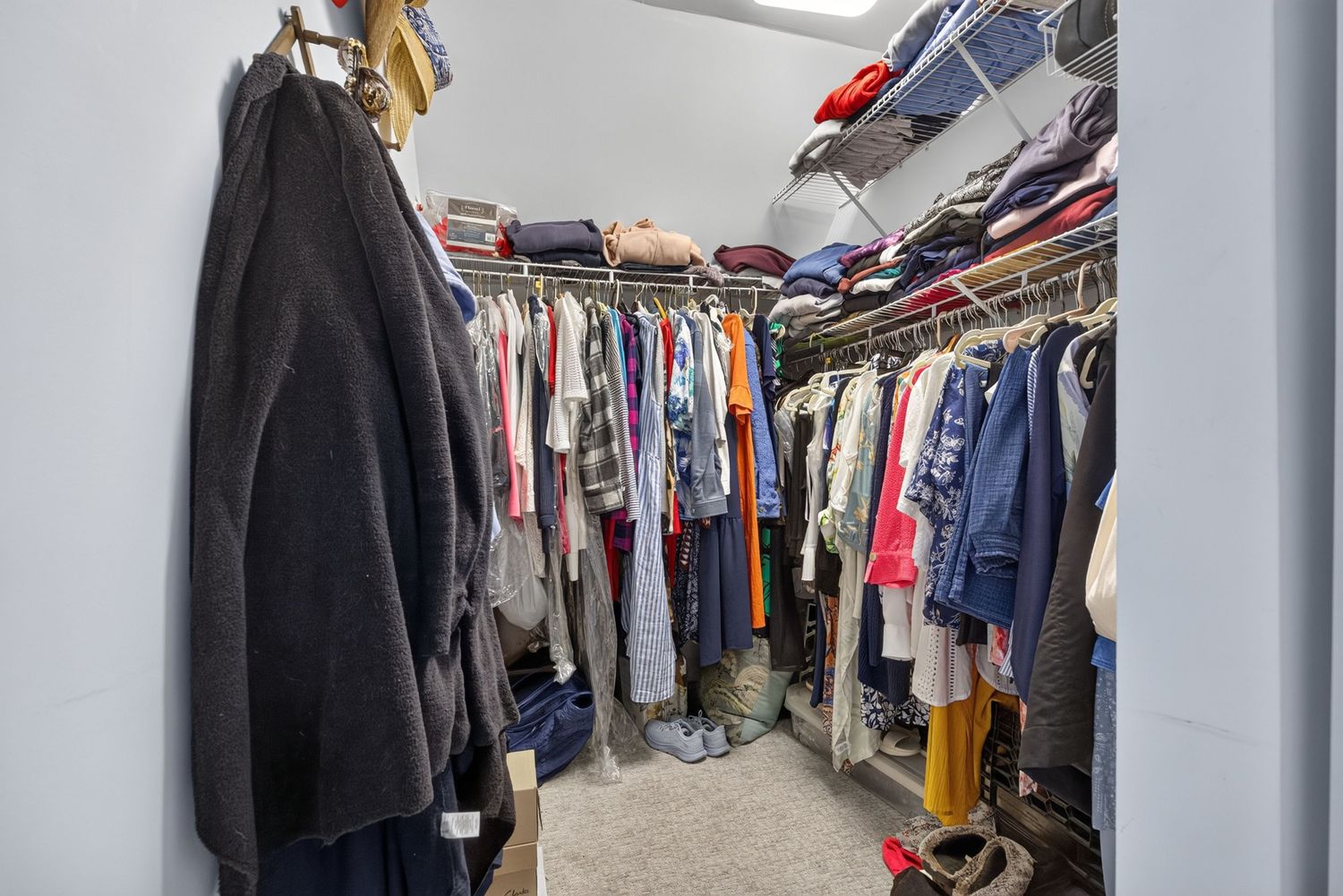 Spacious walk-in closet with double hanging rods filled with clothing on both sides and carpeted flooring.
