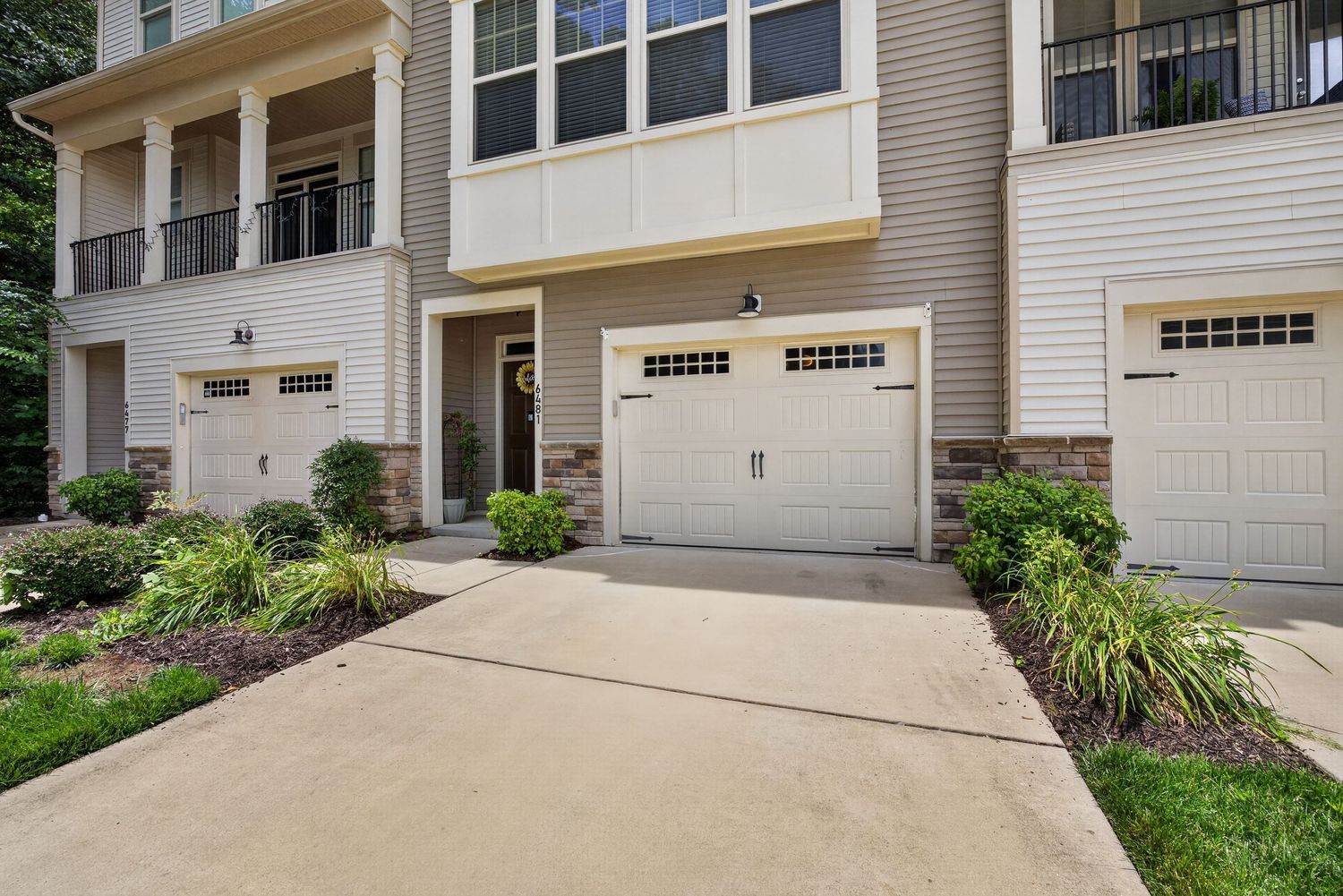 Townhome exterior featuring a white garage door, stone accents, manicured landscaping, and a welcoming entryway on a sunny day.
