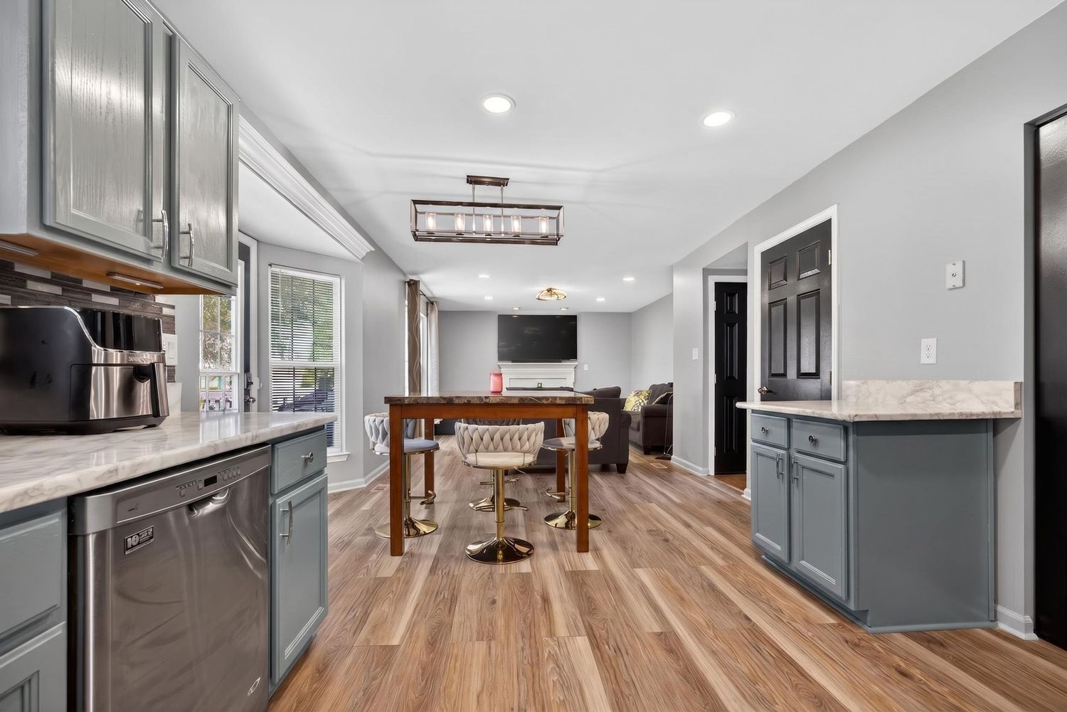 Modern kitchen with gray cabinets, hardwood floors, granite countertops, and open dining area with pendant lighting.