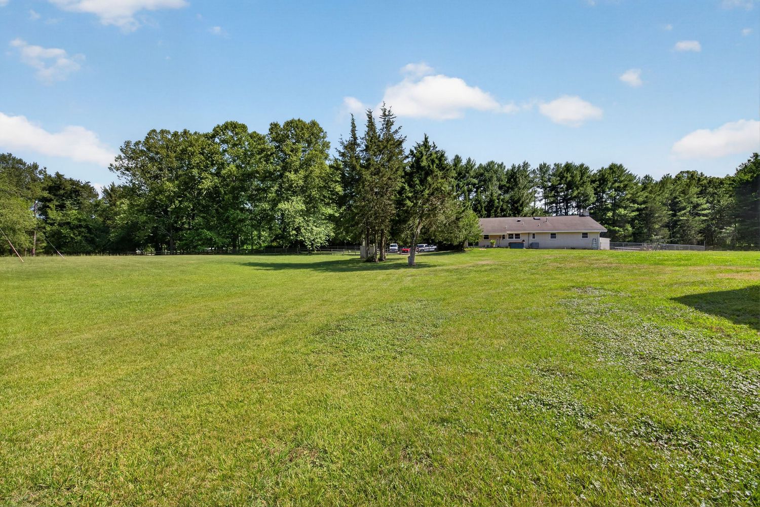 Expansive green lawn with mature trees surrounding a single-story pink home in a peaceful rural setting.