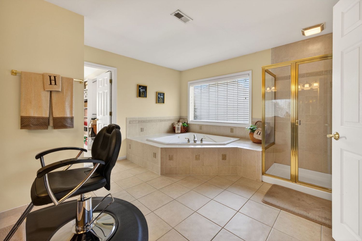 Spacious master bathroom with barber chair, corner jetted tub, walk-in glass shower, and beige tile flooring.