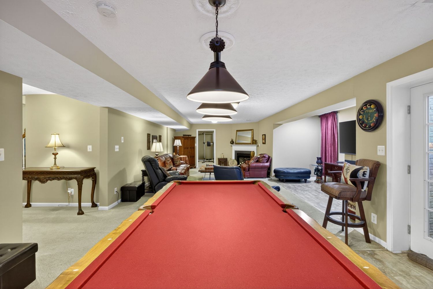Spacious basement game room featuring a red billiard table, pendant lighting, fireplace, and open living area beyond.